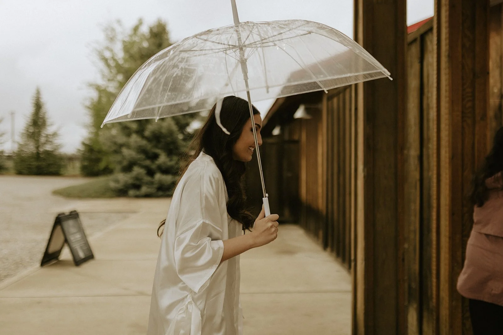 Woman holding a clear umbrella outside a rustic wooden barn winery