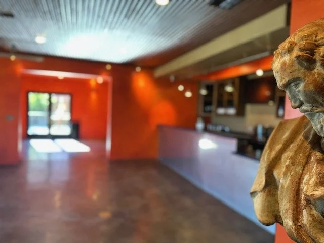 Blurry interior of a room with orange walls, a wooden reception desk, and a sculpture of a woman on the right side.