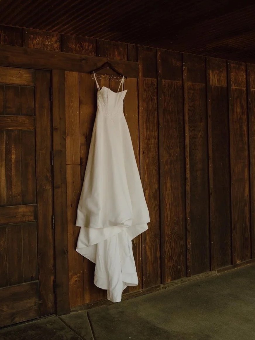 White wedding dress hanging on a rustic wooden barn wall