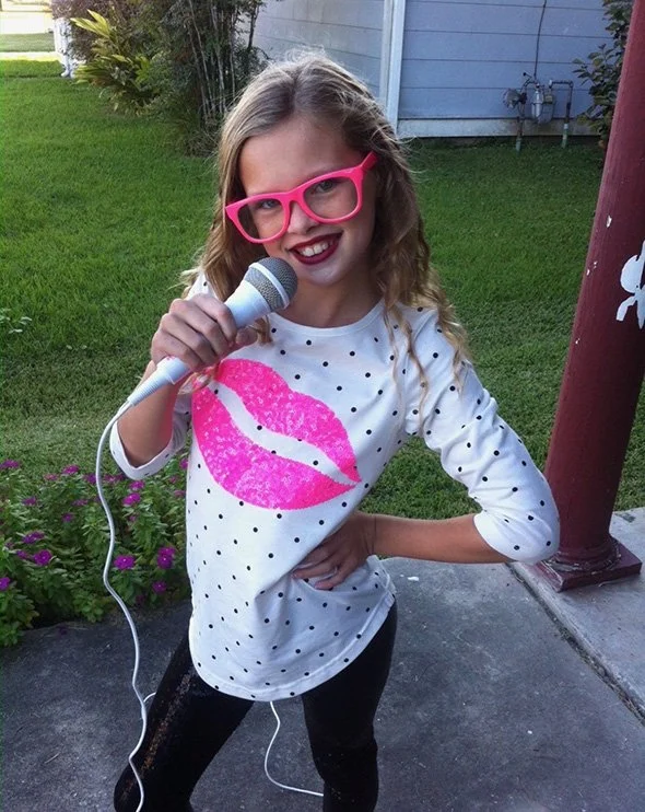 Kenedi at age 7 with big pink glasses and microphone.jpg
