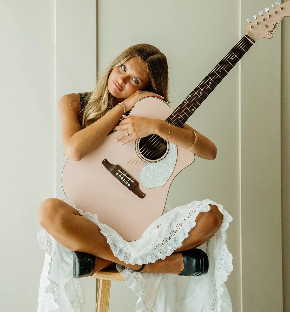 Kenedi hugs her guitar while sitting on a stool.jpg