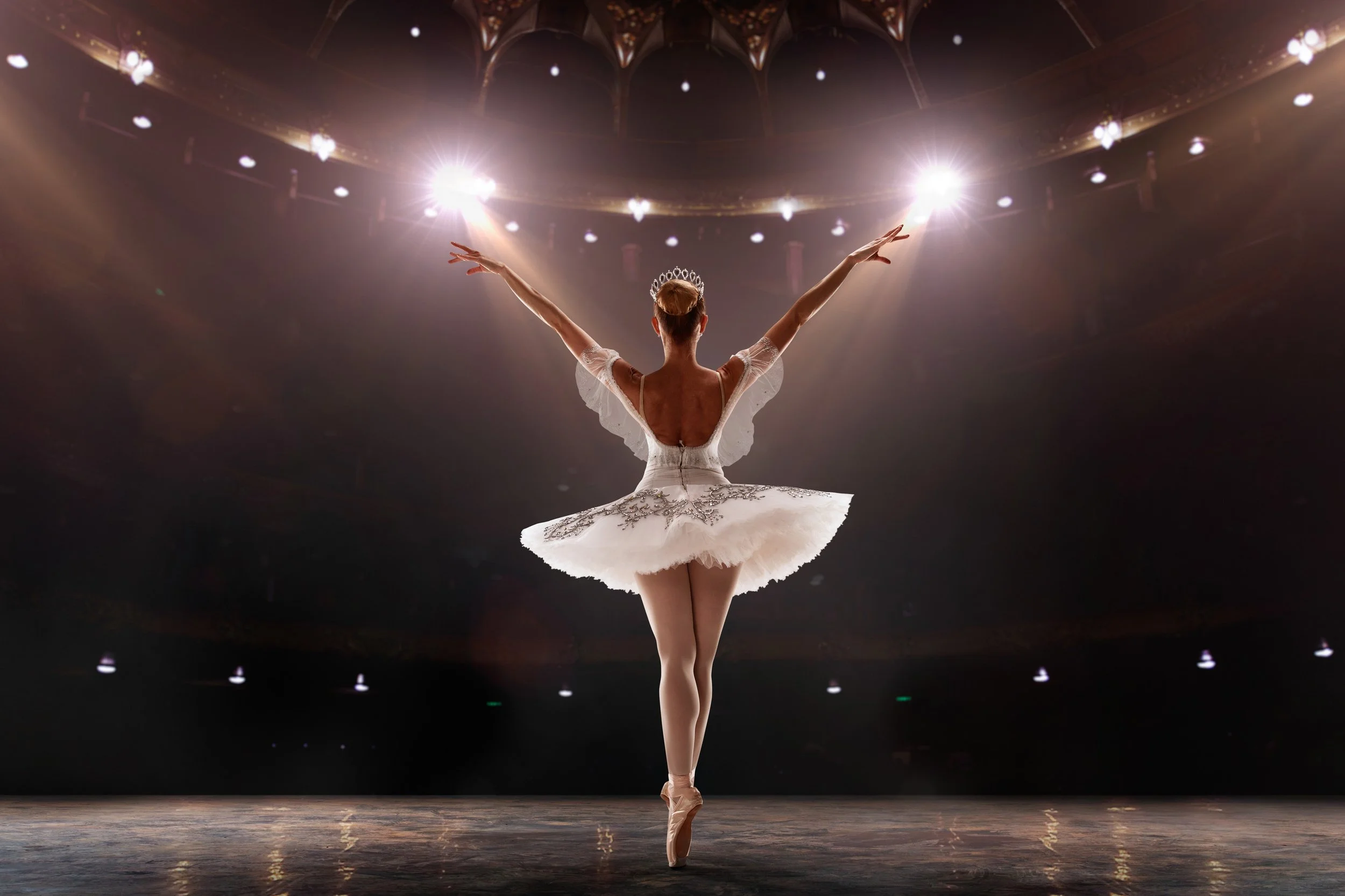 Ballet dancer in a white tutu and tiara on stage with spotlights overhead, representing all the Ballet and Dance dates in Salt Lake City and Utah County.