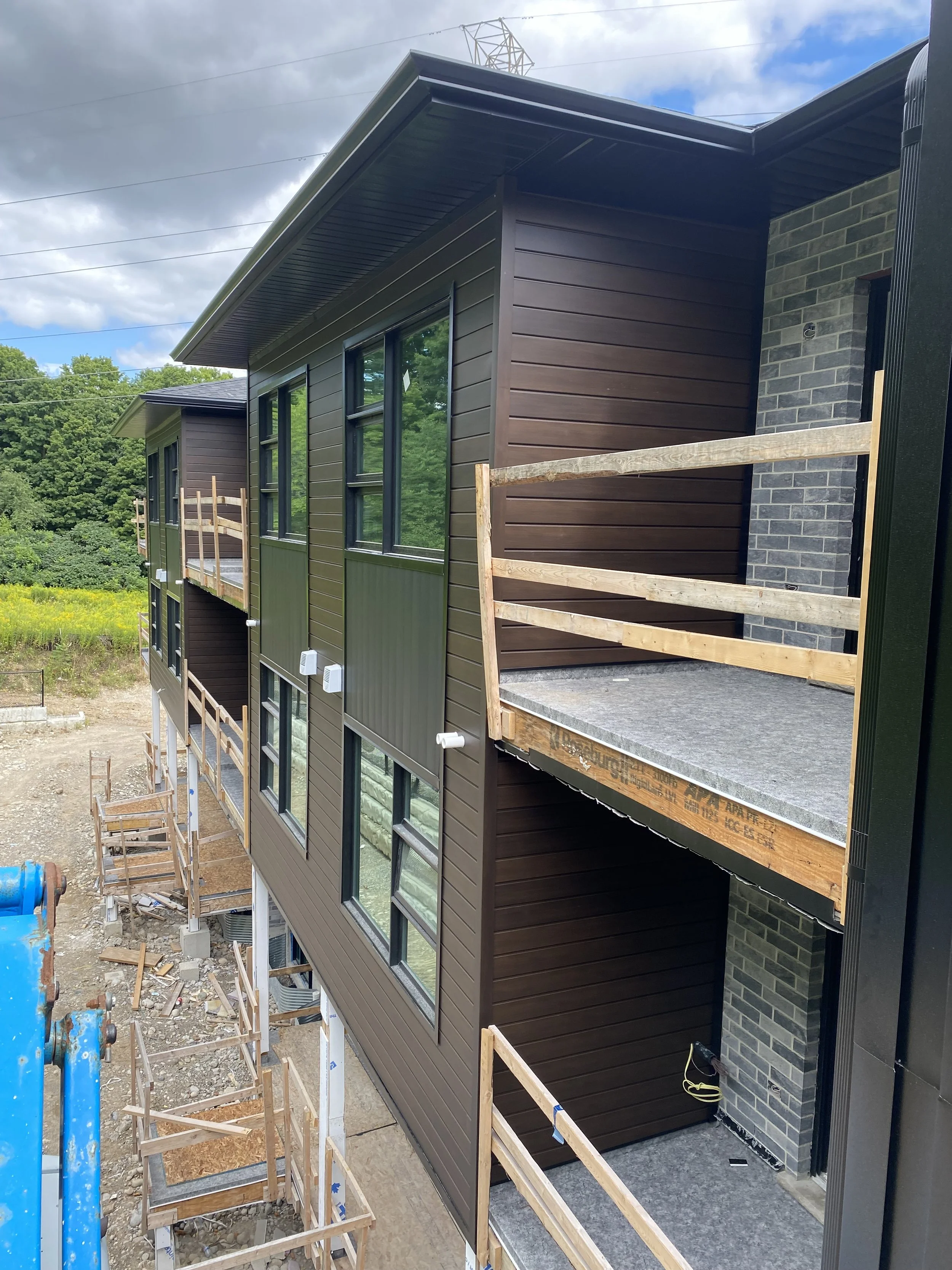 Under construction of a multi-story residential building with brown and green siding, multiple windows, and scaffolding or supports around the exterior.