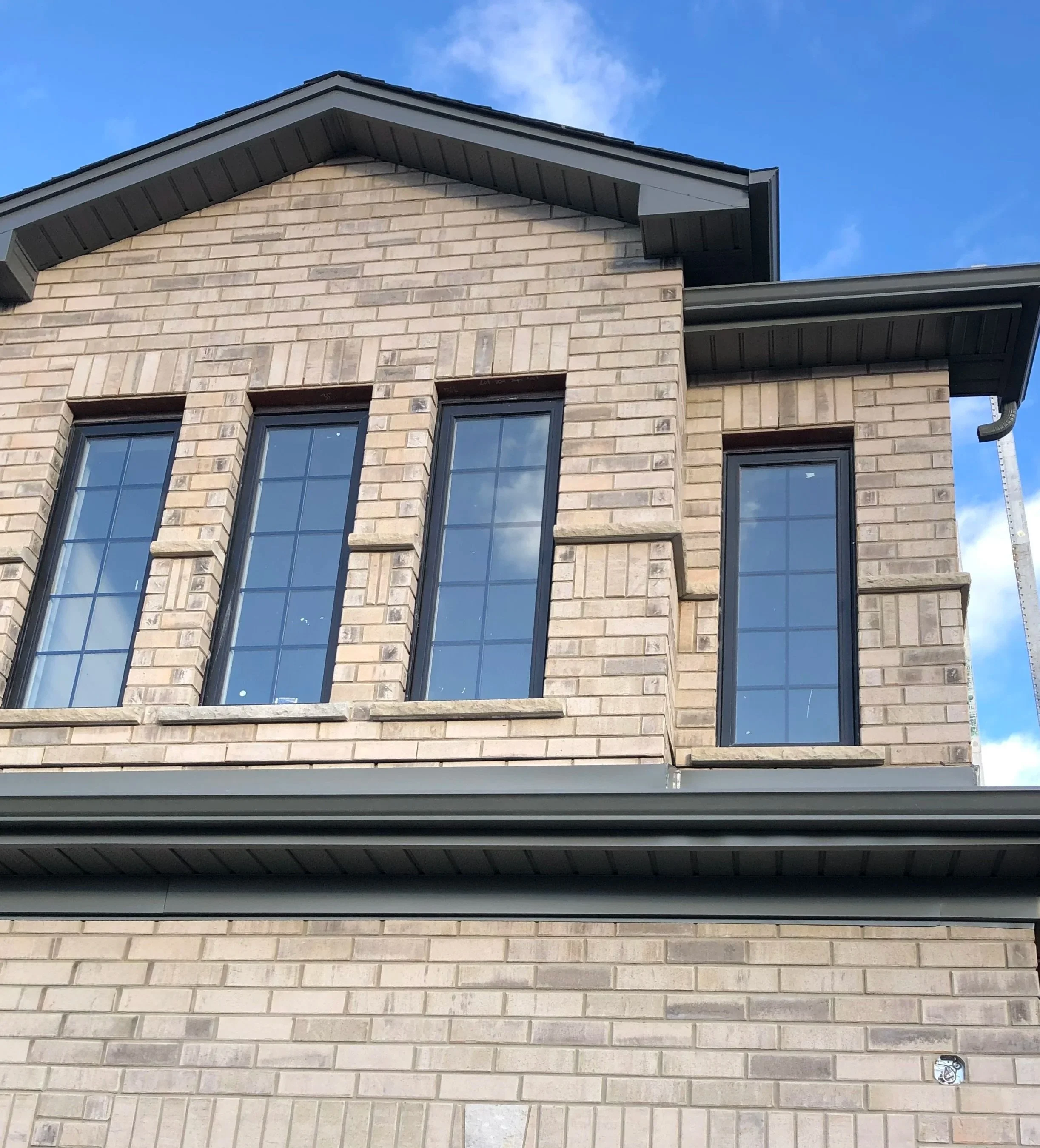 Close-up of a two-story brick house exterior with tall narrow windows, a sloped roof, and a clear blue sky background.