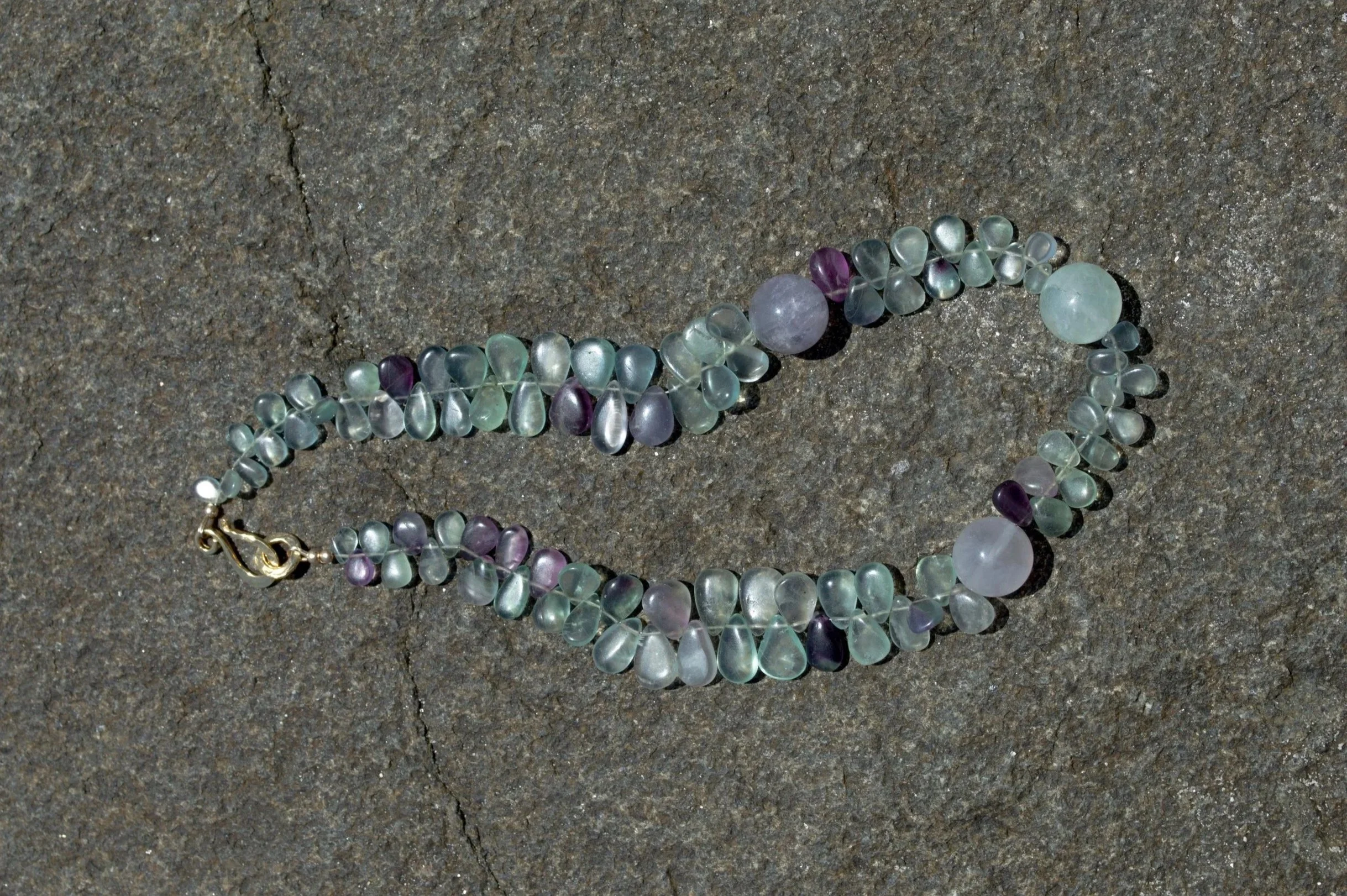 A beaded necklace with pastel-colored beads and a gold clasp, lying on a rough, gray stone surface.