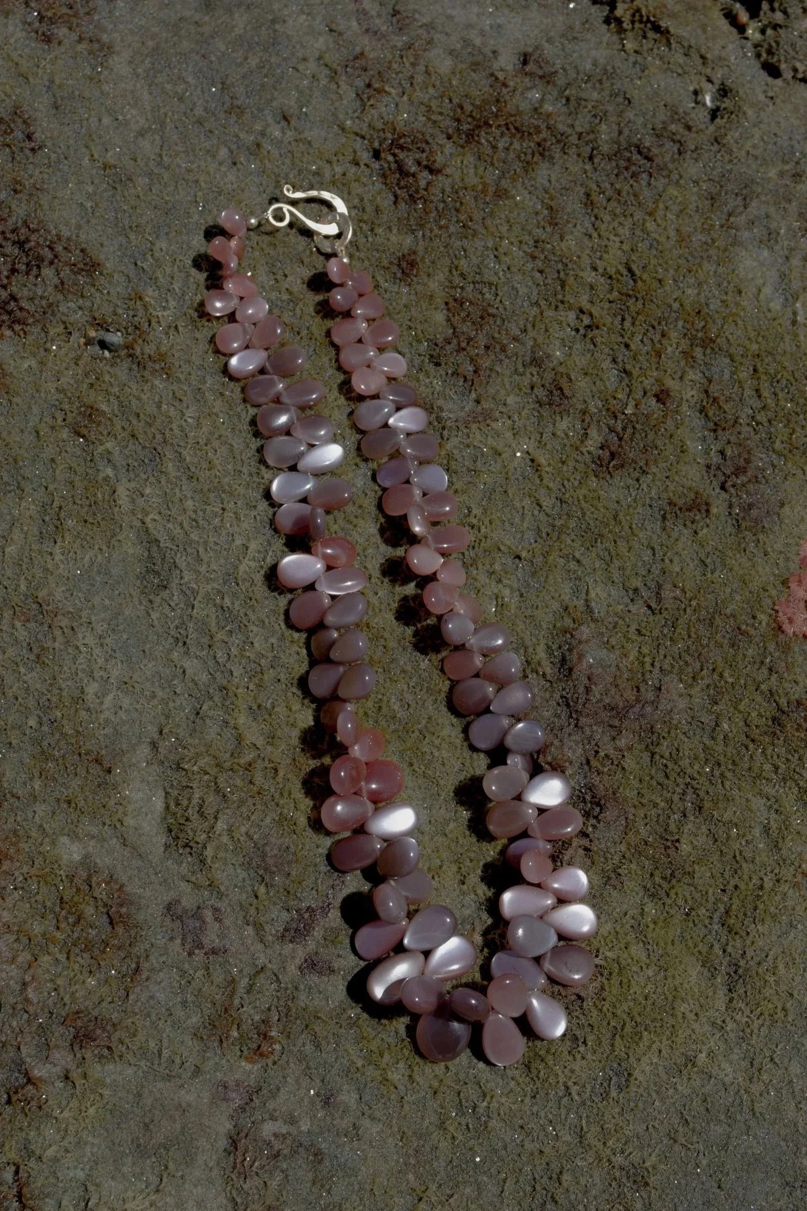 Pink and white shell necklace with a silver clasp lying on sandy ground.