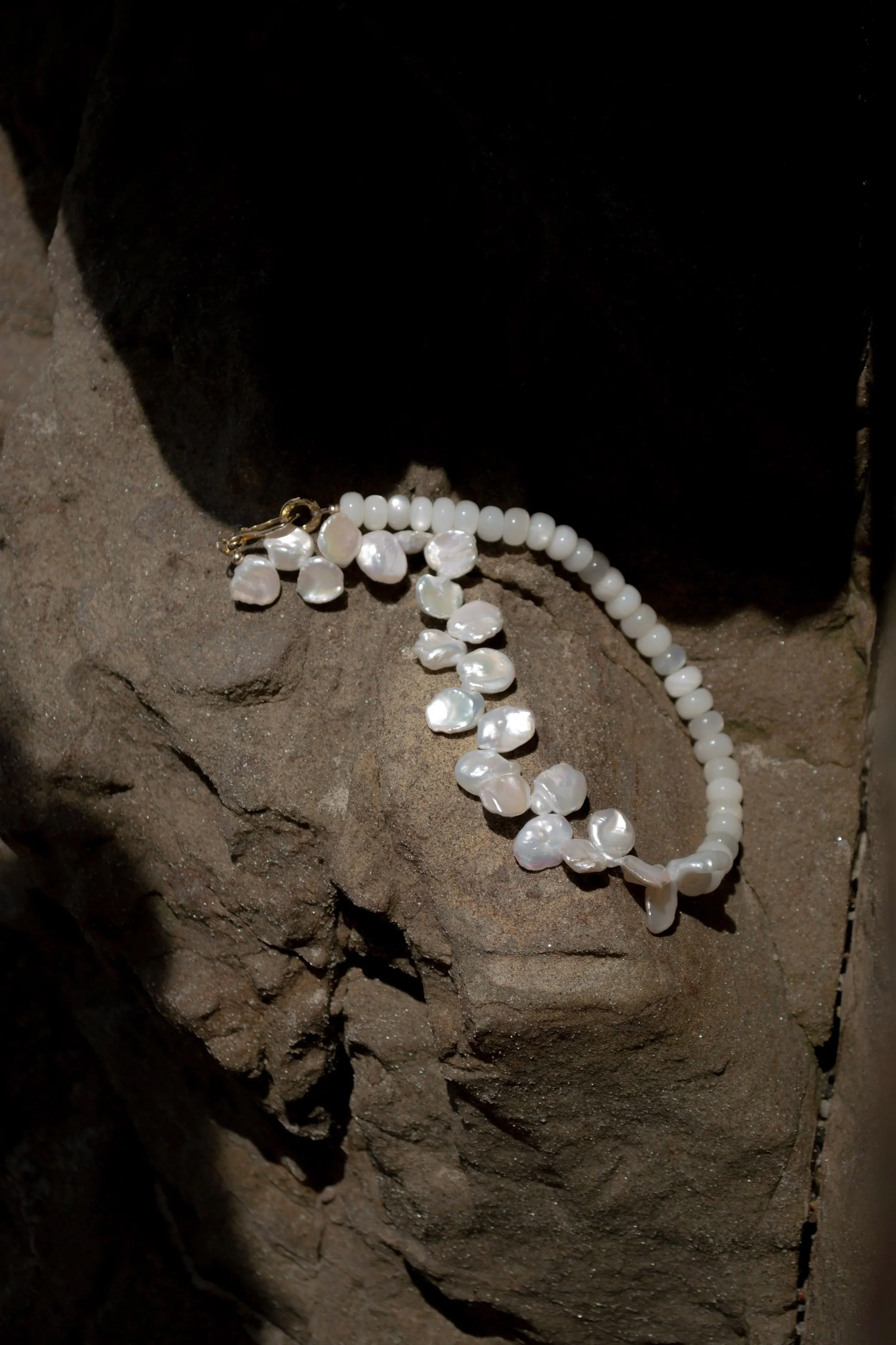 A pearl necklace and dangling earrings with white stones resting on a rough stone surface.