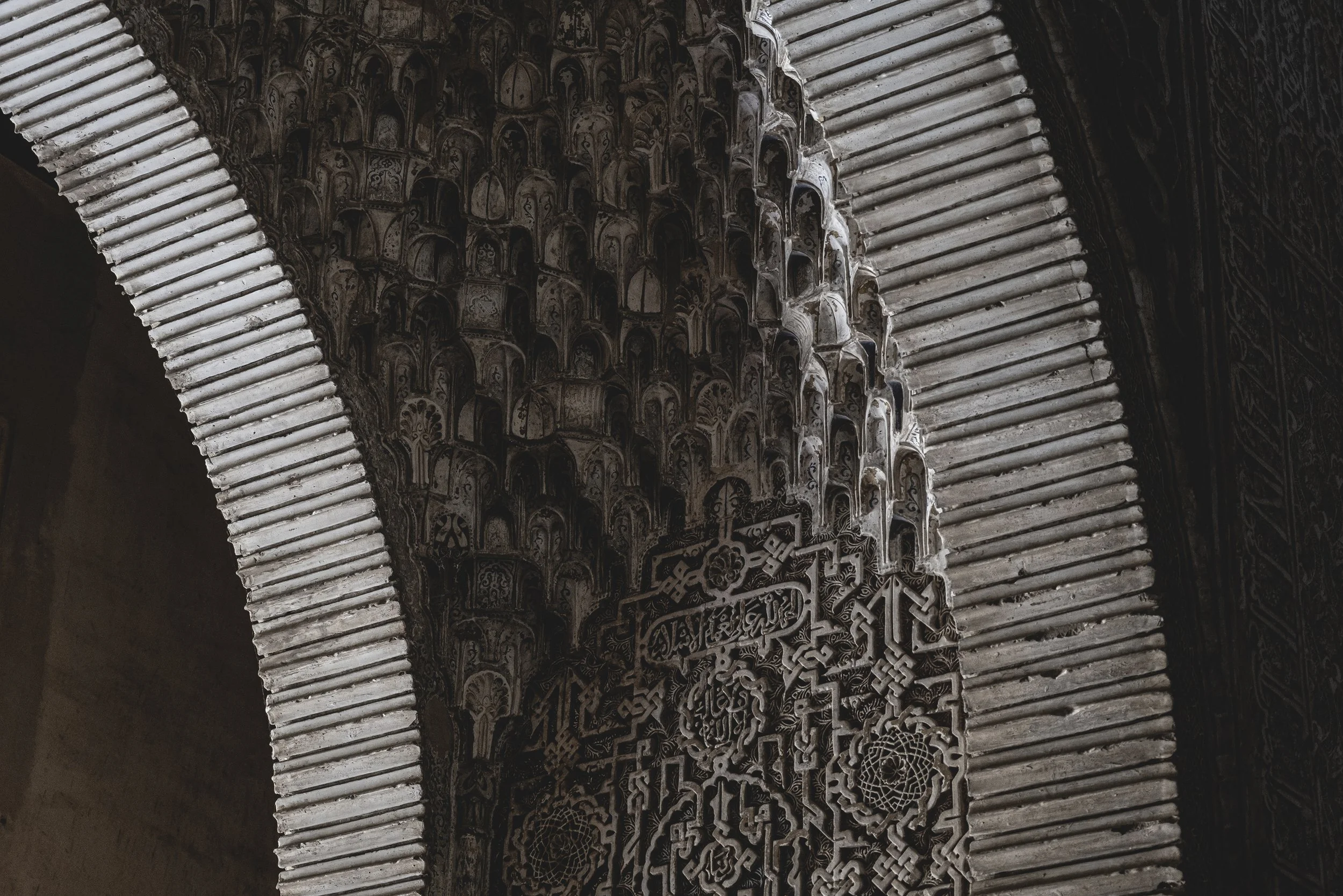 Détail d'une arche en pierre avec une décoration complexe en relief, typique de l'architecture islamique, avec motifs géométriques et calligraphiques.