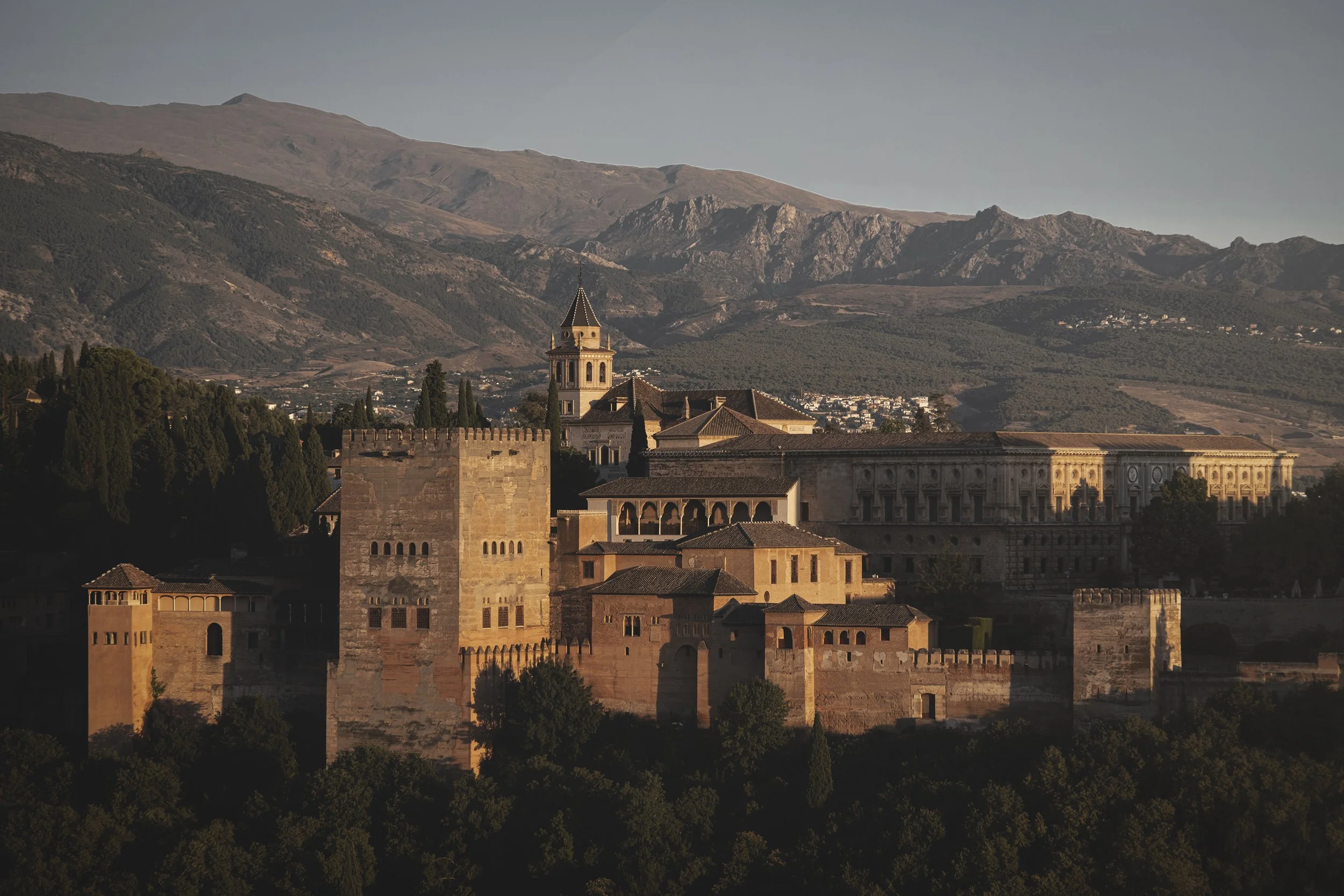 Vue du Alhambra, ancien palais et forteresse à Grenade, Espagne, avec montagnes en arrière-plan au coucher du soleil.