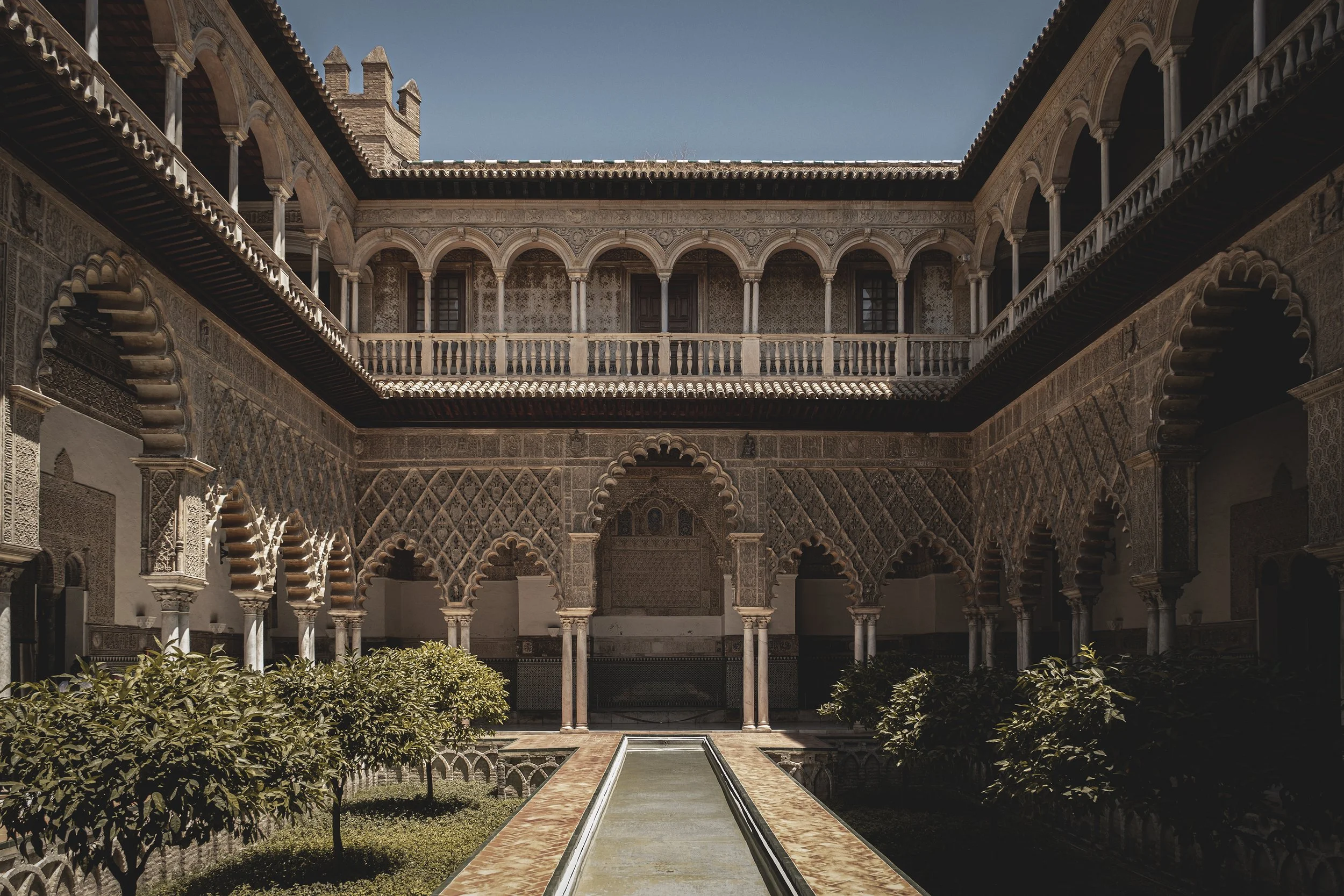 Cours intérieure avec fontaine, entourée de murs ornés de motifs islamiques, avec deux niveaux de galeries en arcades et balustrades.