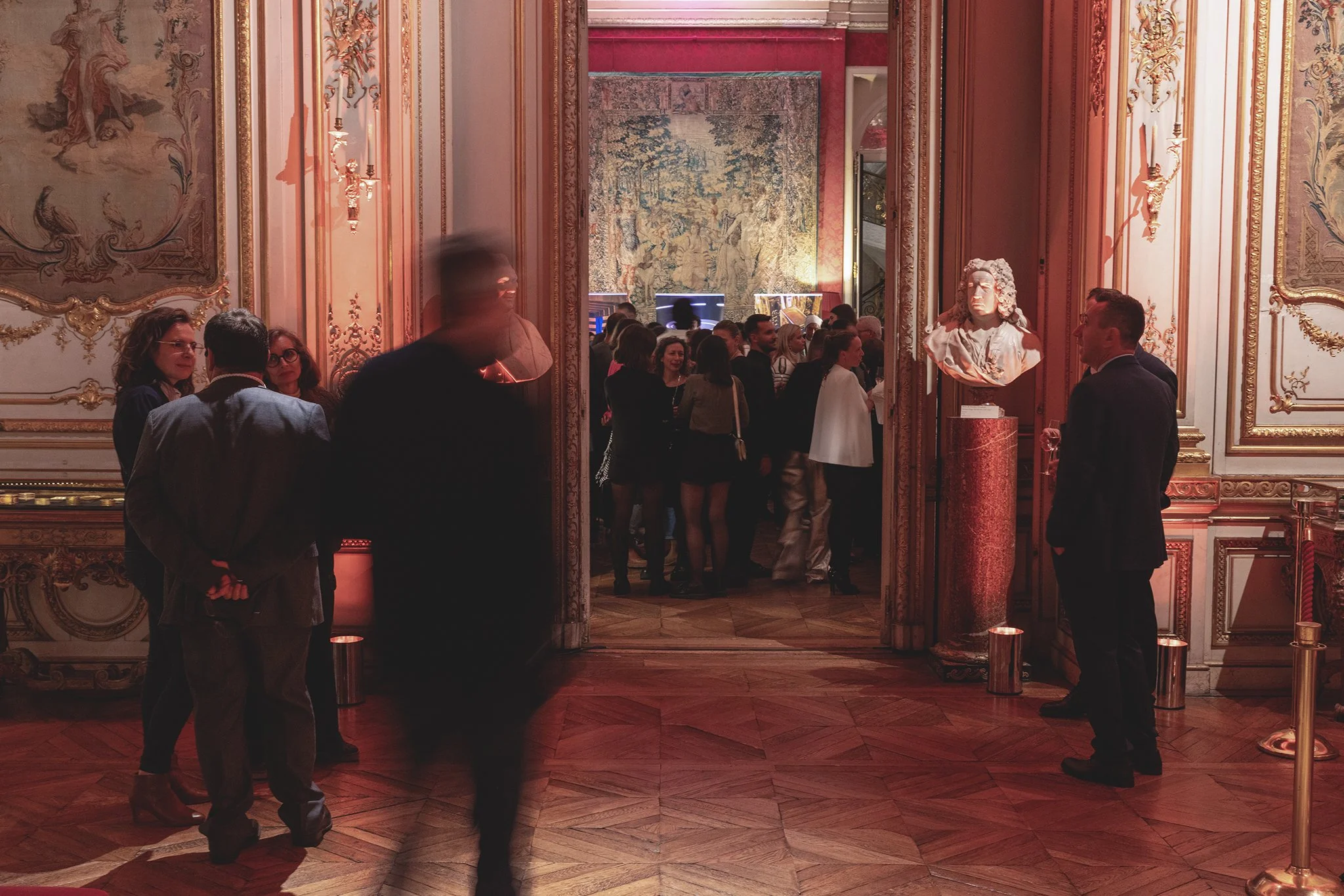 Groupe de personnes dans une salle somptueuse avec des murs ornés de dorures et d'œuvres d'art, scène d'un événement ou d'une réception élégante.