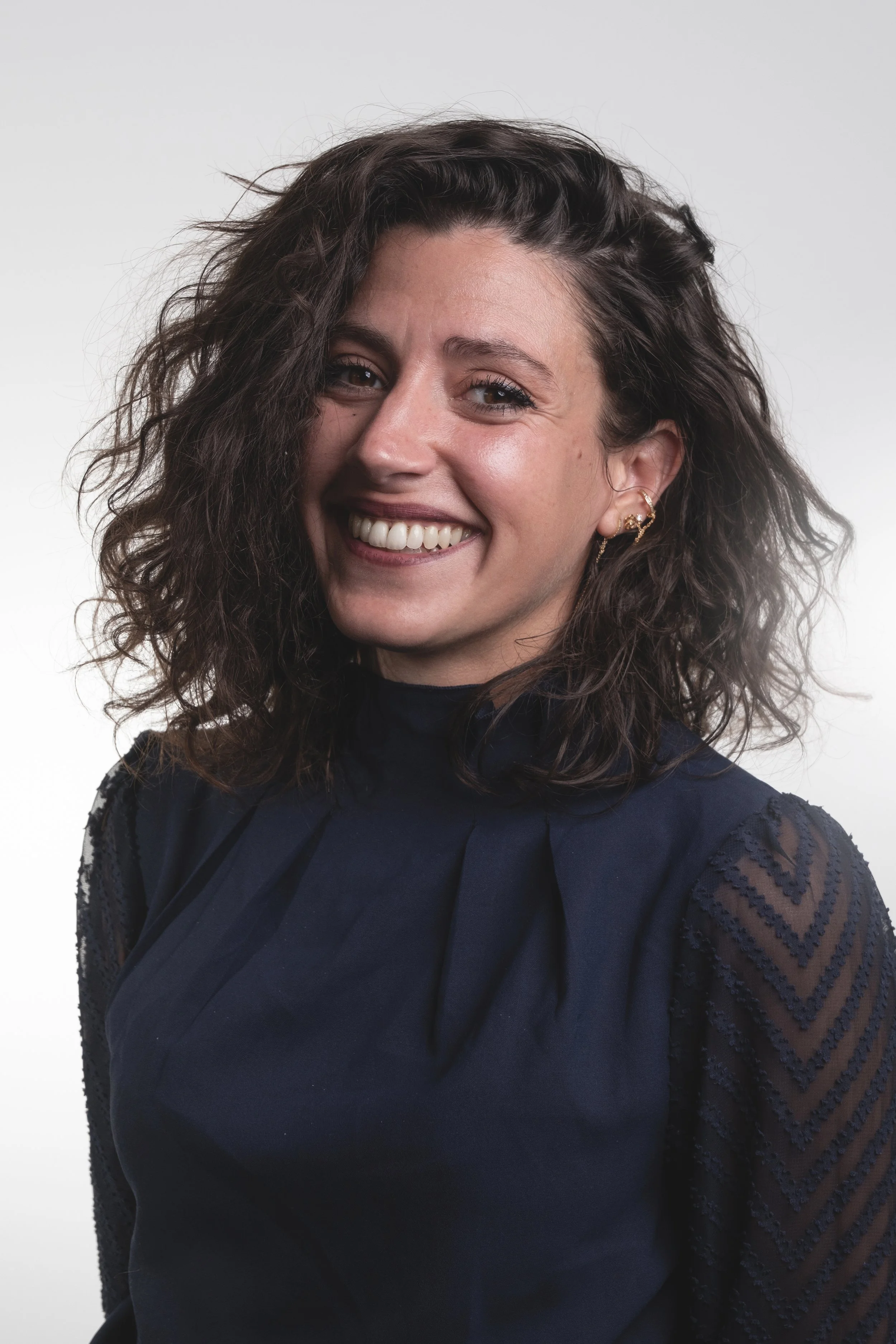 Portrait d'une femme souriante avec des cheveux bouclés, portant un haut noir, contre un fond blanc.