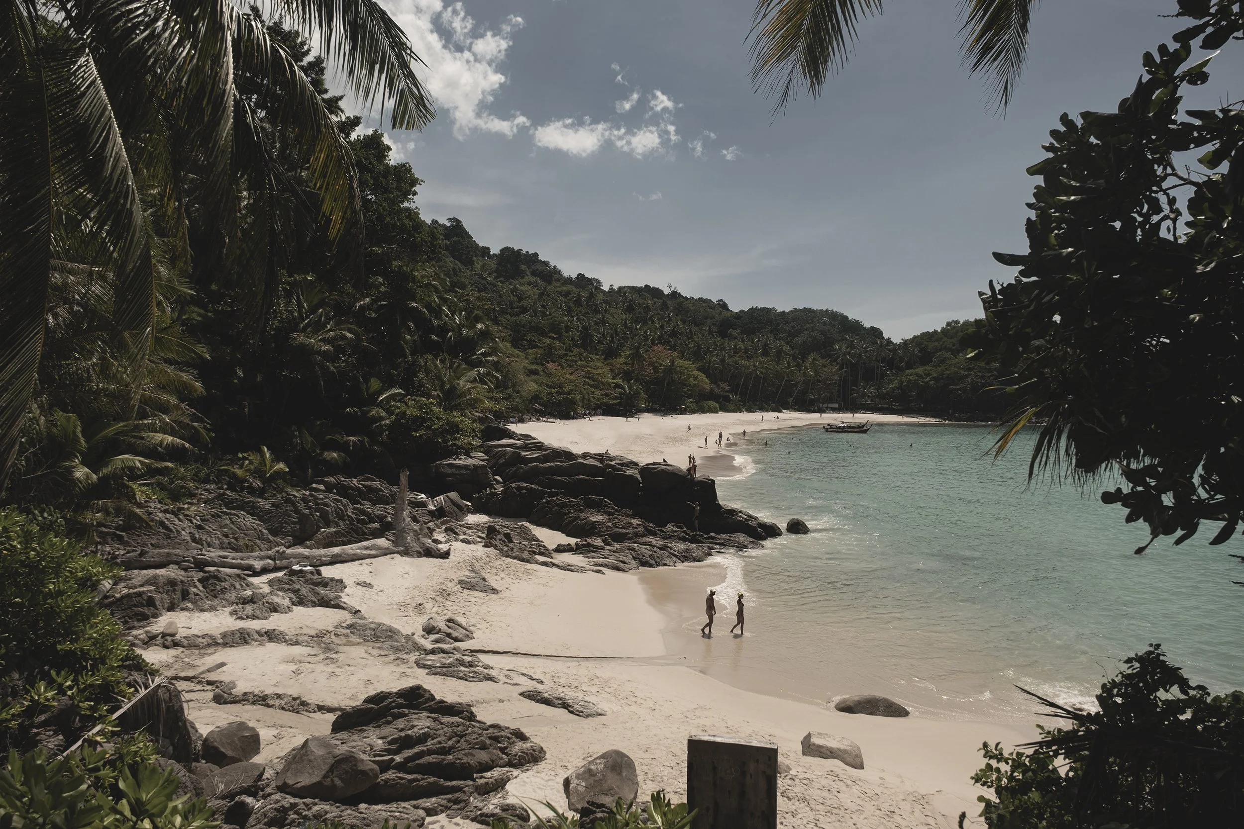 Plage isolée avec sable blanc, rochers, eau claire, entourée de végétation tropicale.