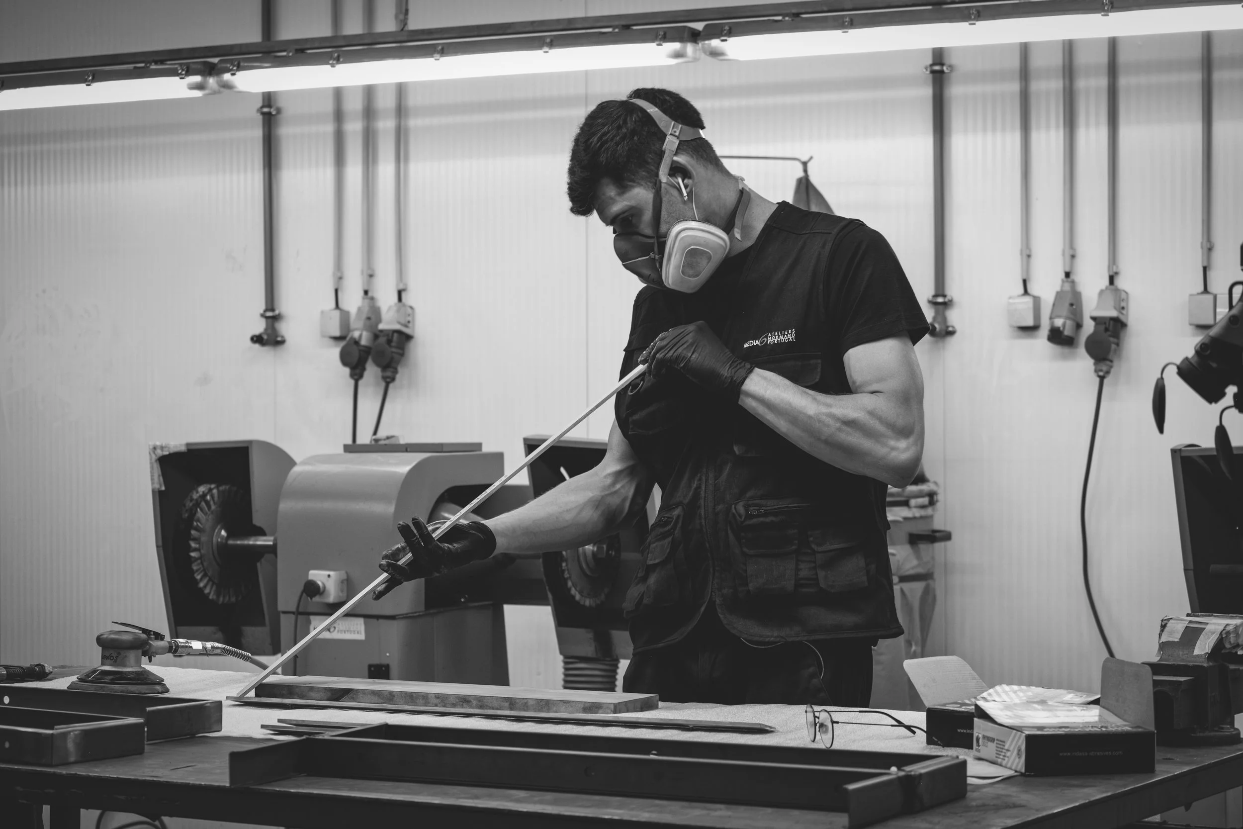 Un homme travaille dans un atelier avec des équipements industriels, portant un masque, des gants et utilisant un outil.