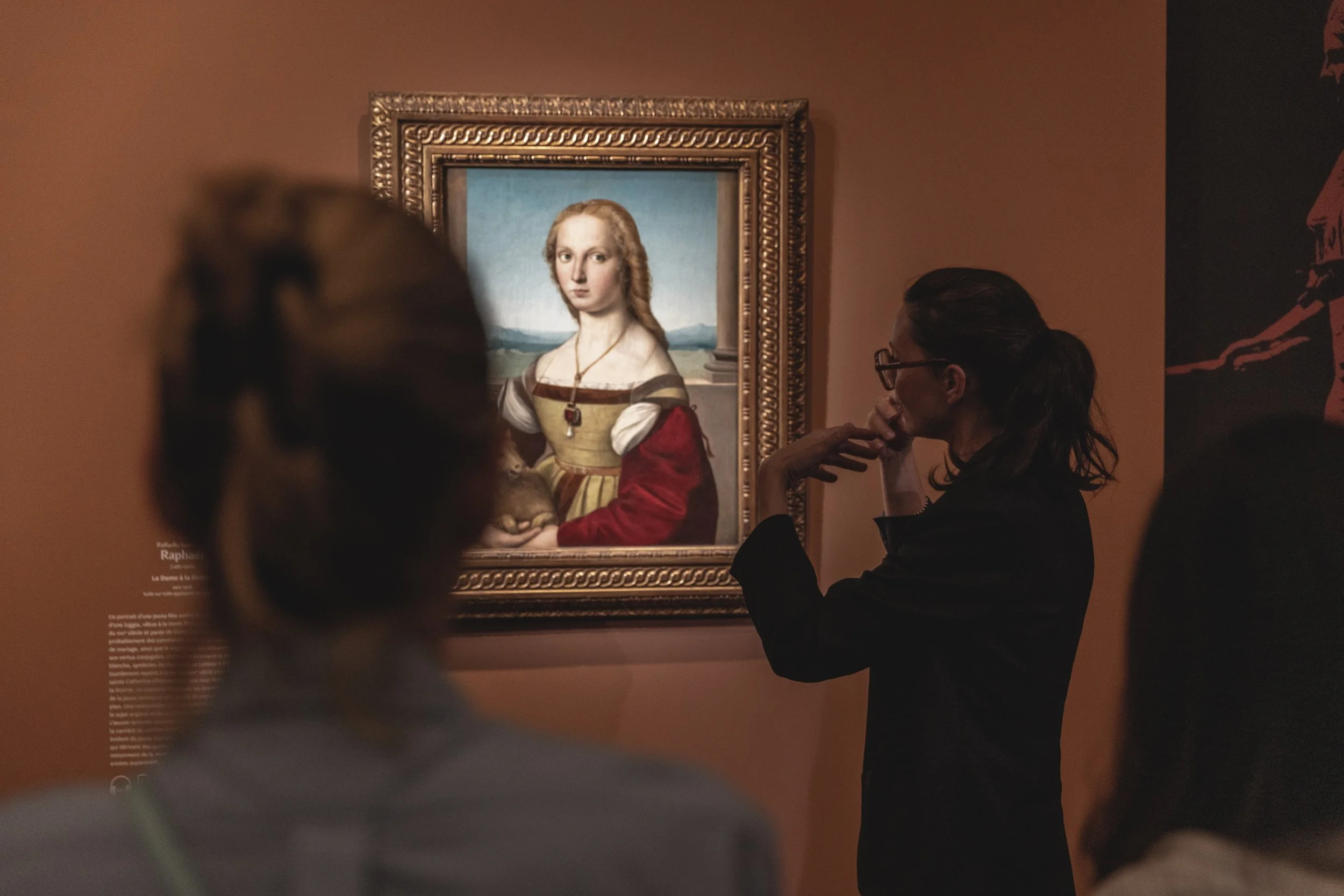 Une femme regarde une peinture de la Joconde dans un musée, entourée d'autres visiteurs.