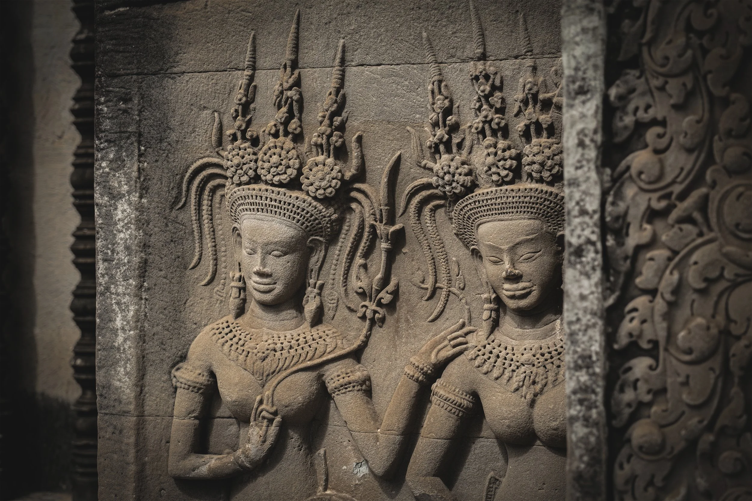 sculpture en pierre représentant deux figures féminines avec des coiffures ornées et des colliers, probablement une œuvre ancienne de style khmer.