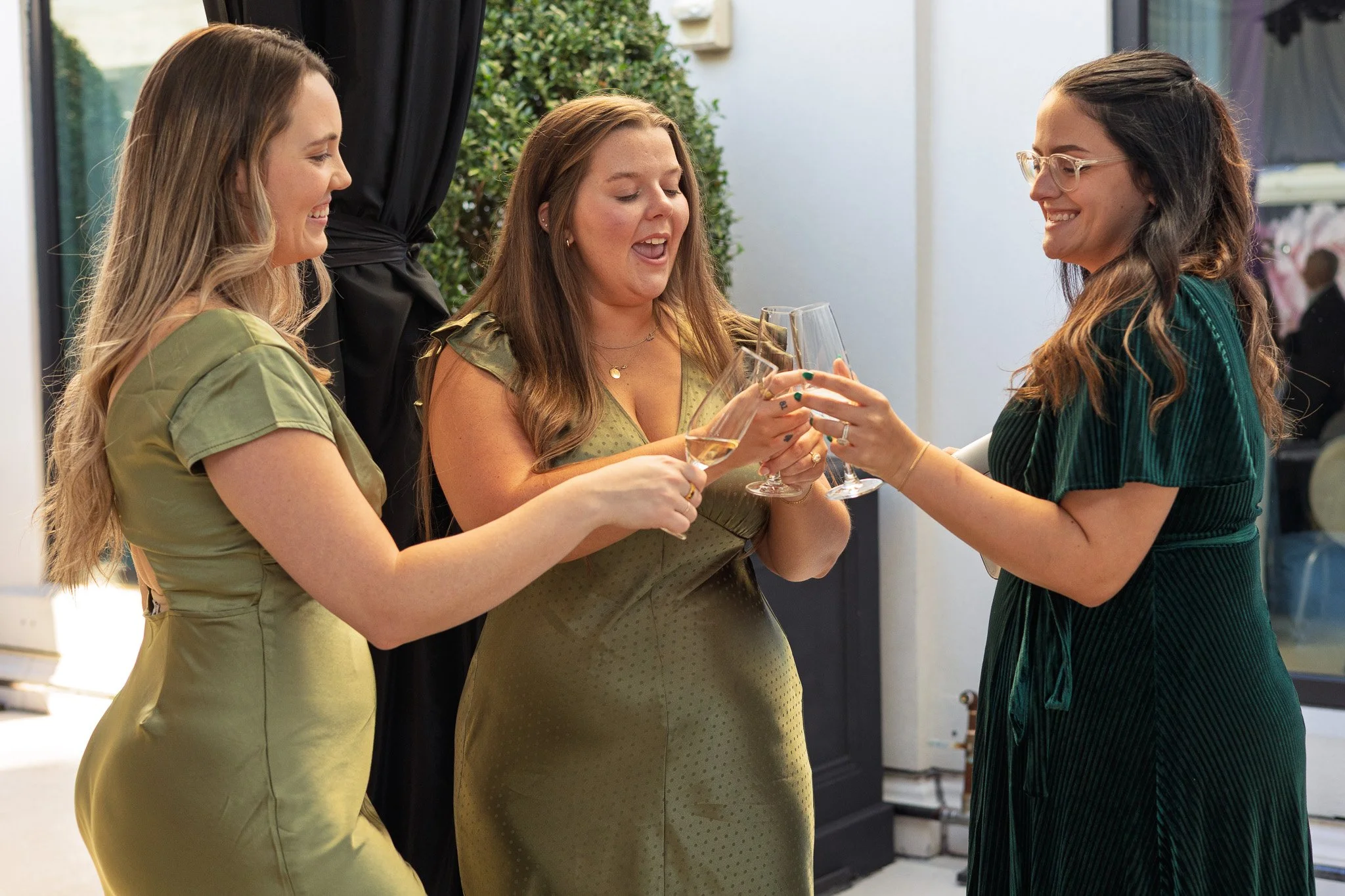 Three women smiling and clinking champagne glasses at a celebration or party.