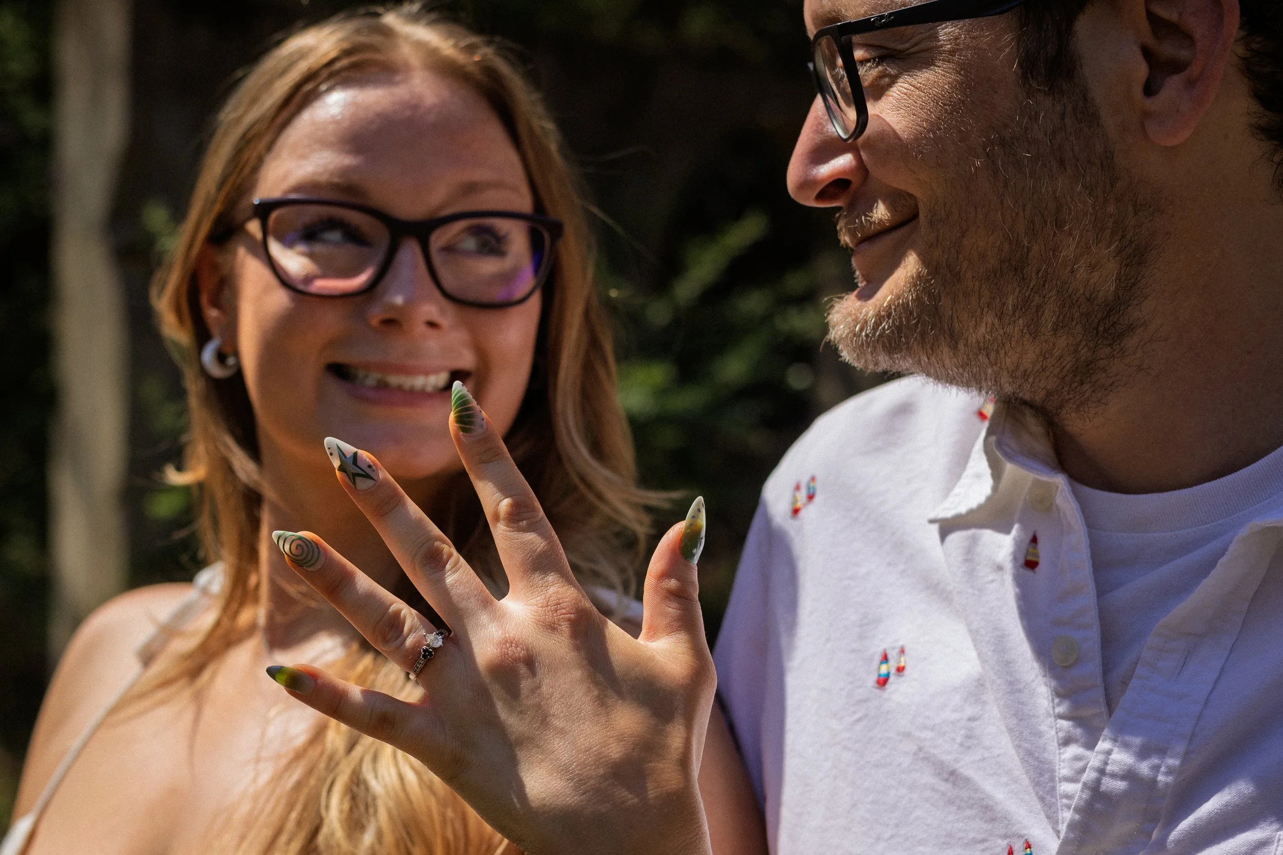 A woman with glasses showing her manicured hand with colorful nail art as a man smiling at her