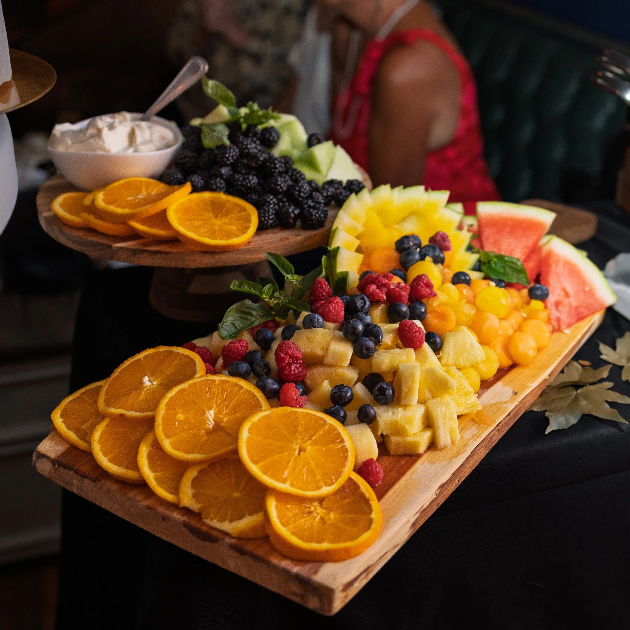 Assorted fresh cut fruits including orange slices, watermelon, pineapple, berries, and honeydew melon arranged on a wooden serving tray.