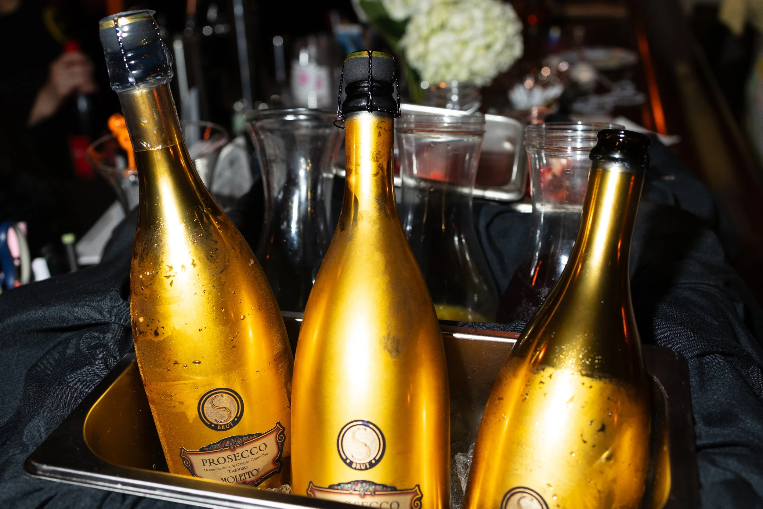 A collection of gold-colored bottles of sparkling wine or champagne in an ice bucket at a party or celebration.