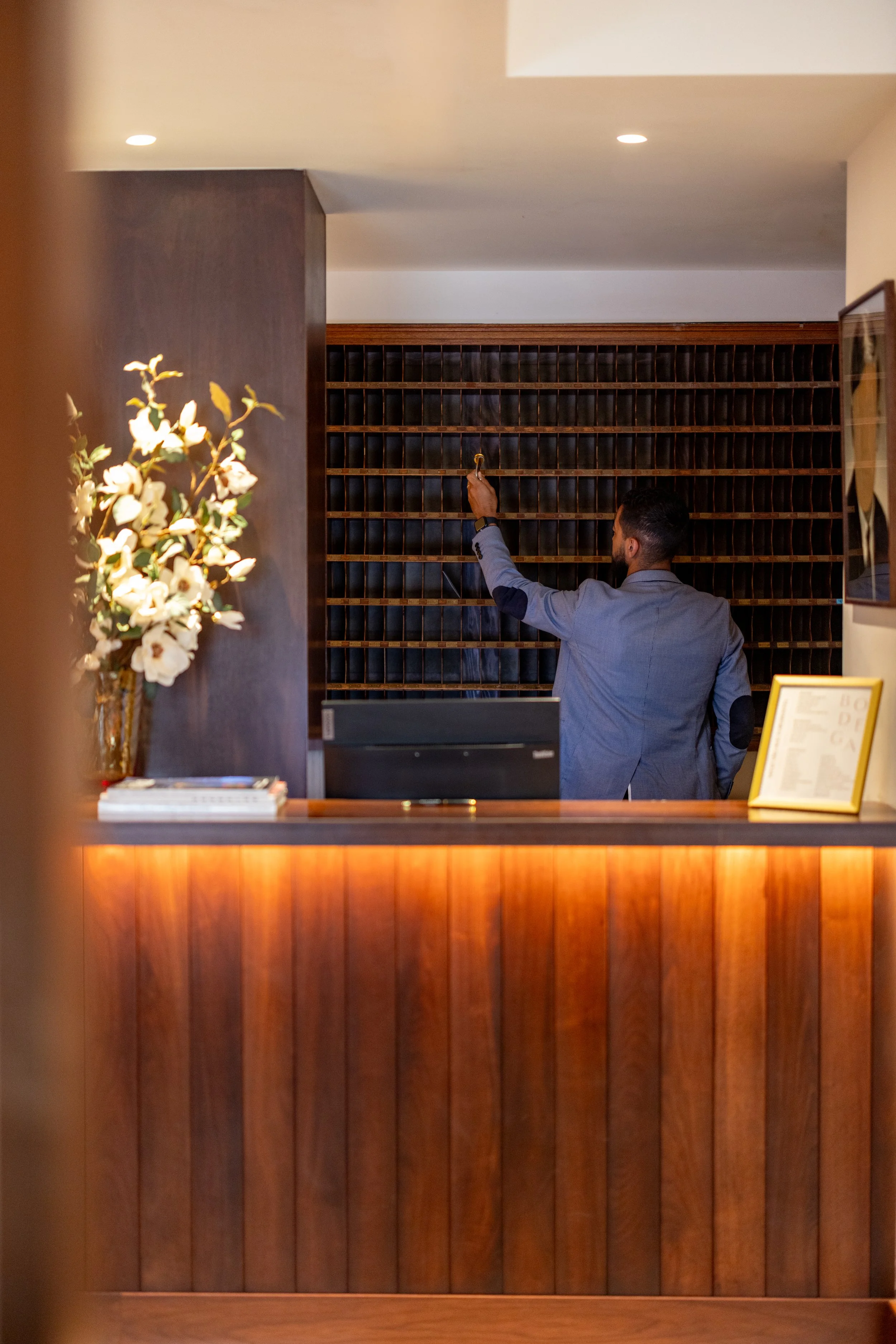 A man in a gray suit is reaching for a key or a small object on a decorative wooden lattice wall in a hotel lobby or reception area.