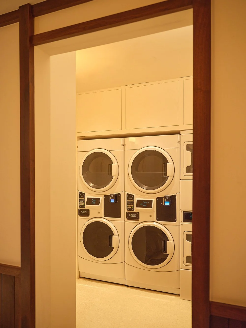 View through a doorway showing four stacked front-load washing machines in a laundry room.