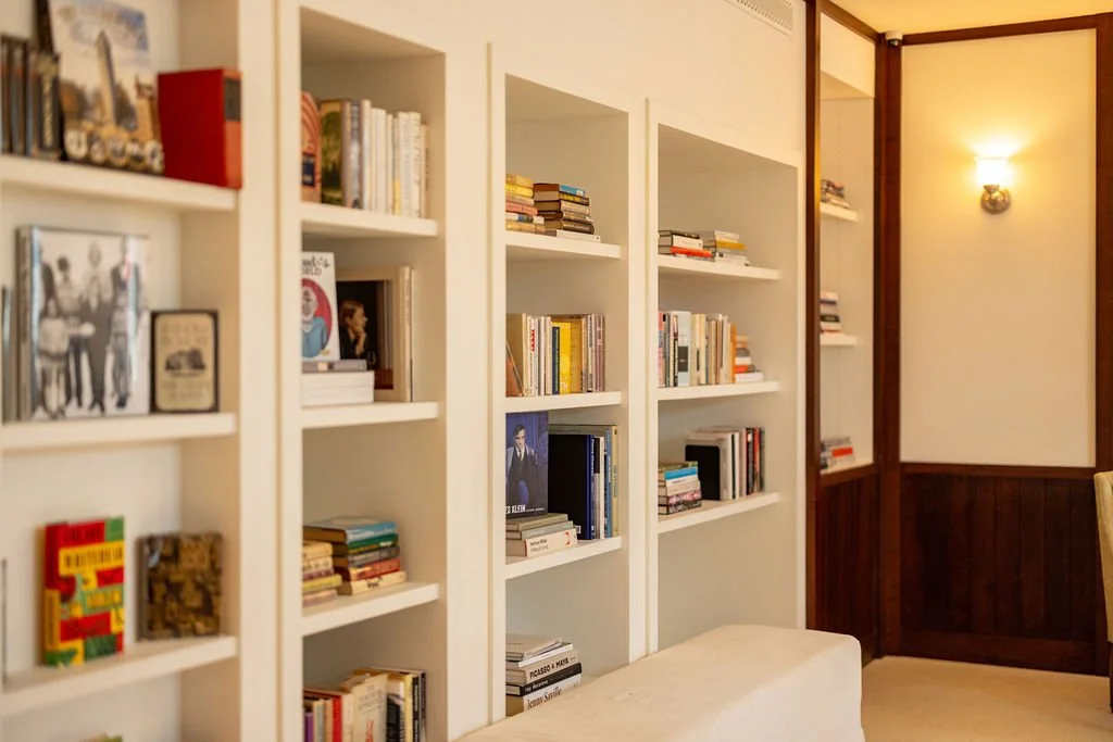 A cozy reading nook with white built-in bookshelves filled with books, and a warm wall sconce light fixture on the wall.