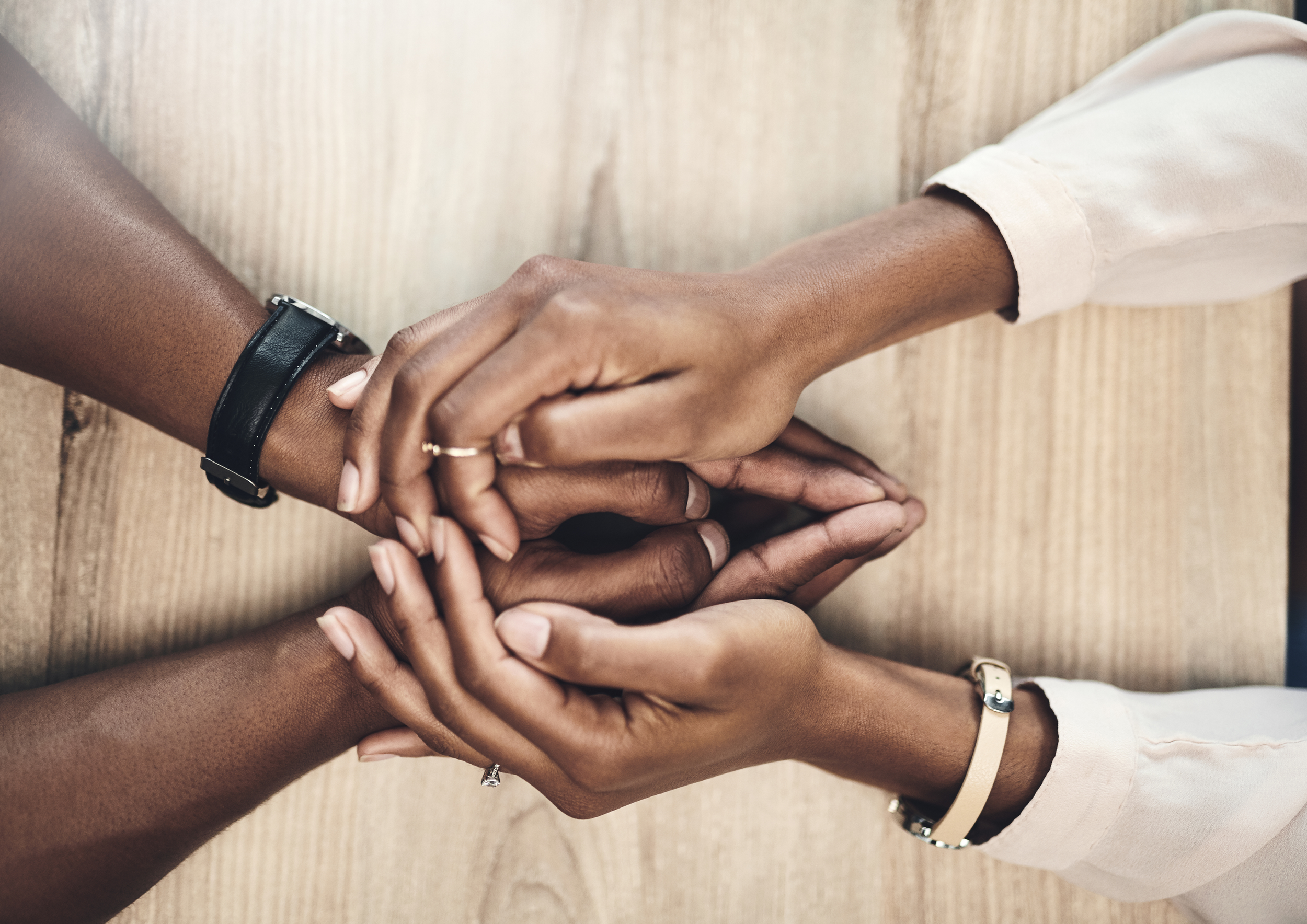 Multiple hands of different skin tones stacked together on a wooden surface, symbolizing unity and teamwork.