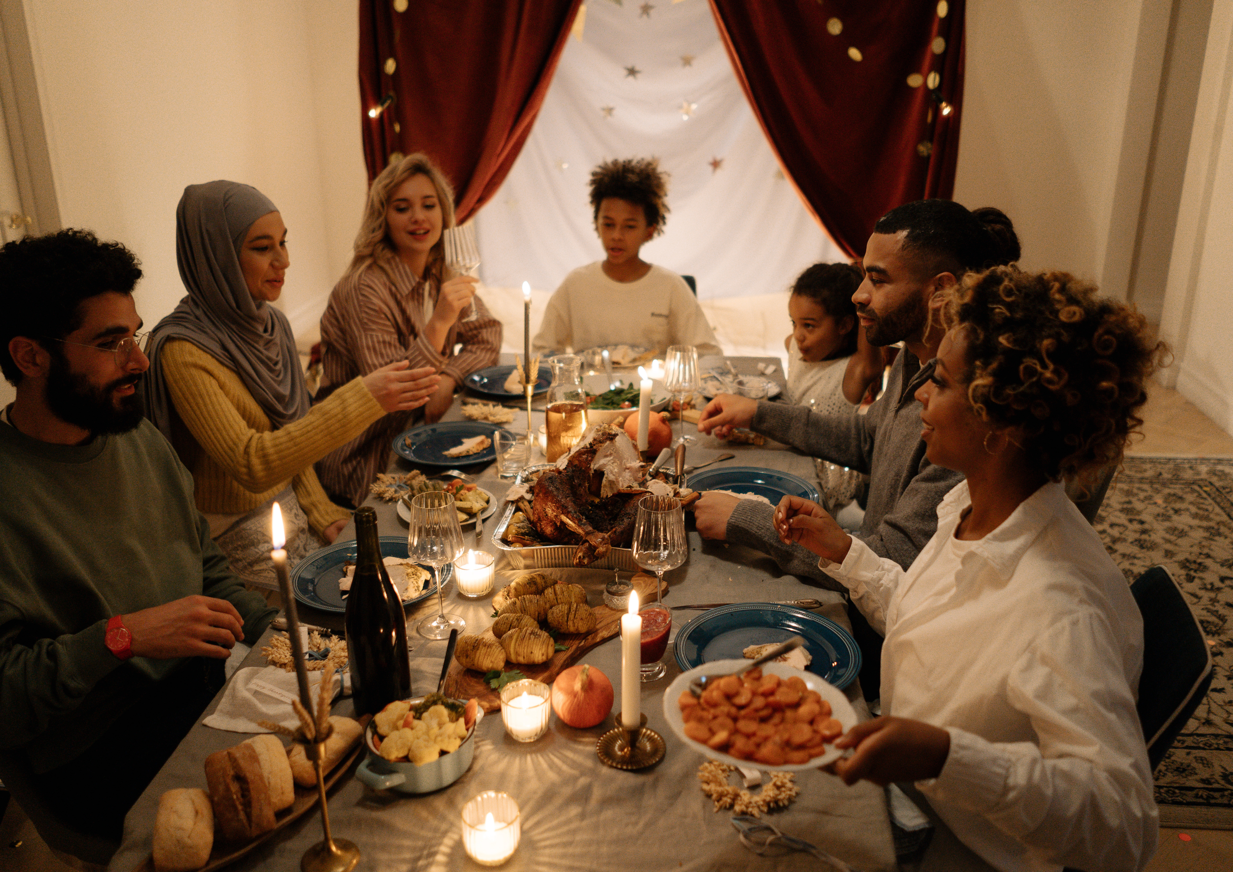 People gathered around a dinner table with Christmas decorations, sharing a meal with a roasted turkey, vegetables, bread, and drinks, celebrating a festive occasion.