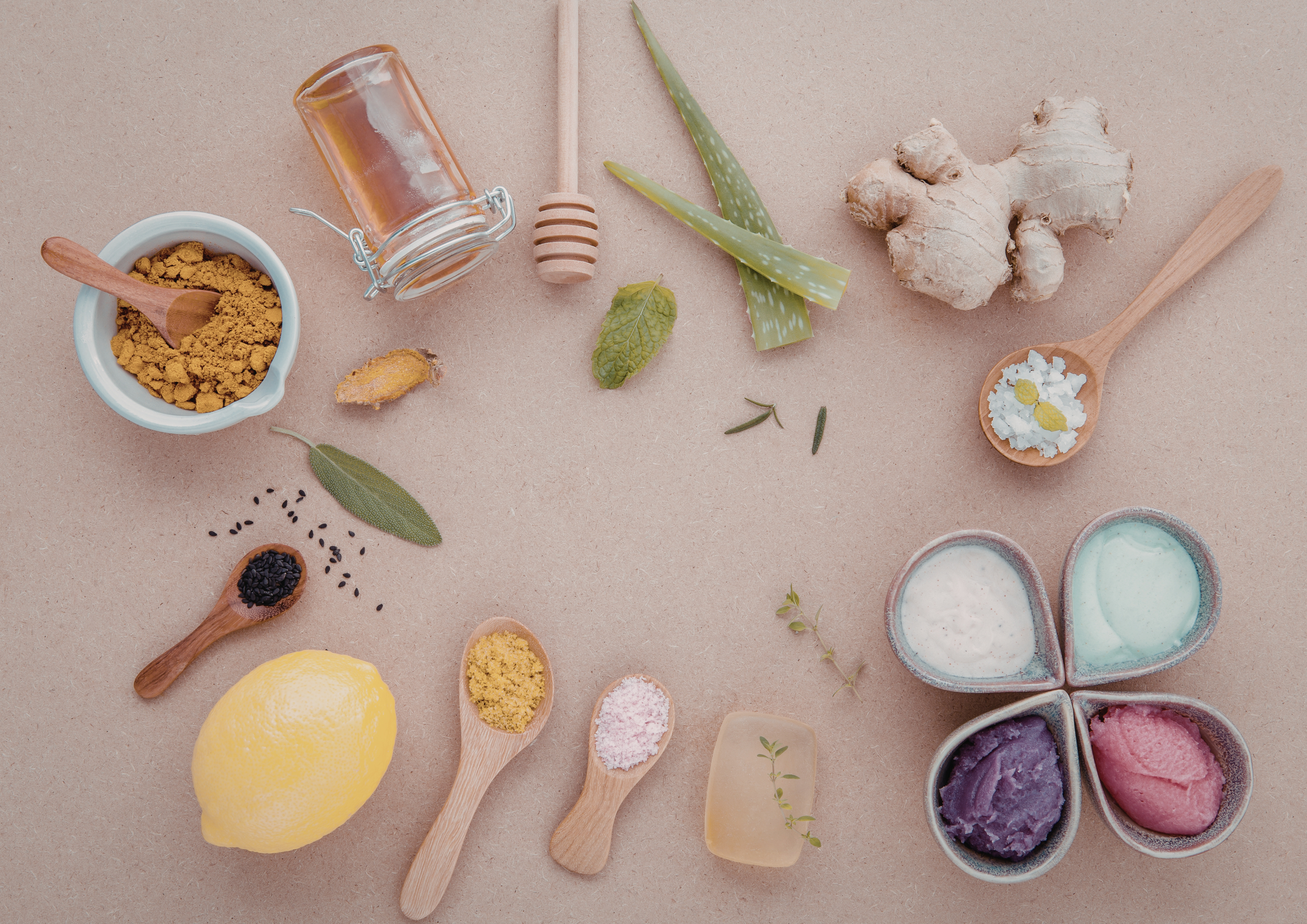 Assorted natural ingredients including ginger root, aloe vera leaves, lemon, honey, turmeric powder, black sesame seeds, pink Himalayan salt, and various herbs on a textured surface, along with small bowls of colorful ice creams.