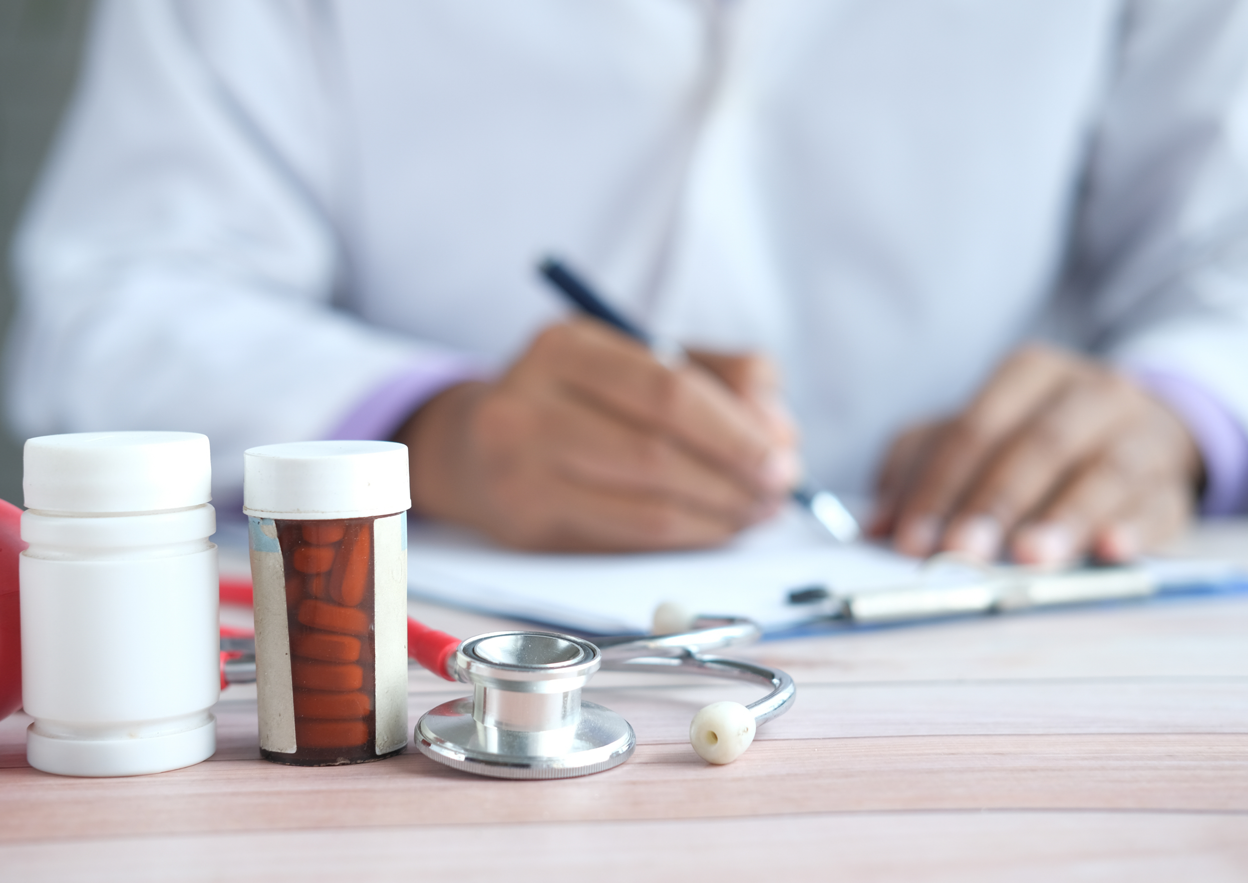 Medicine bottles, a stethoscope, and a physician writing notes on a clipboard