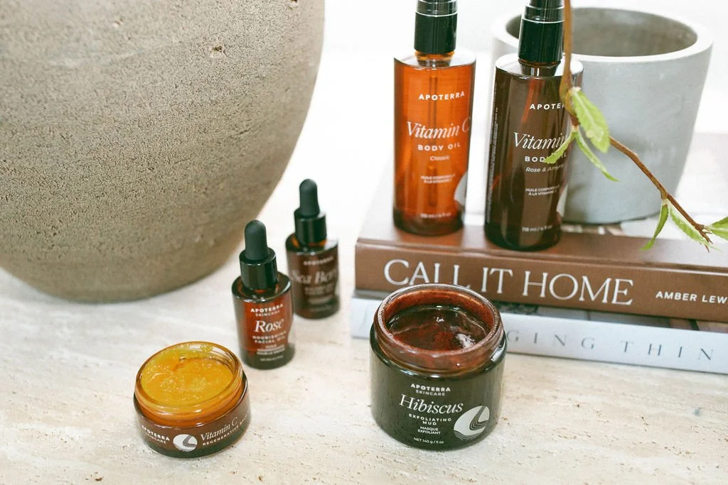Spa products on a white surface, including body oils, a mask, and dropper bottles, with books in the background.