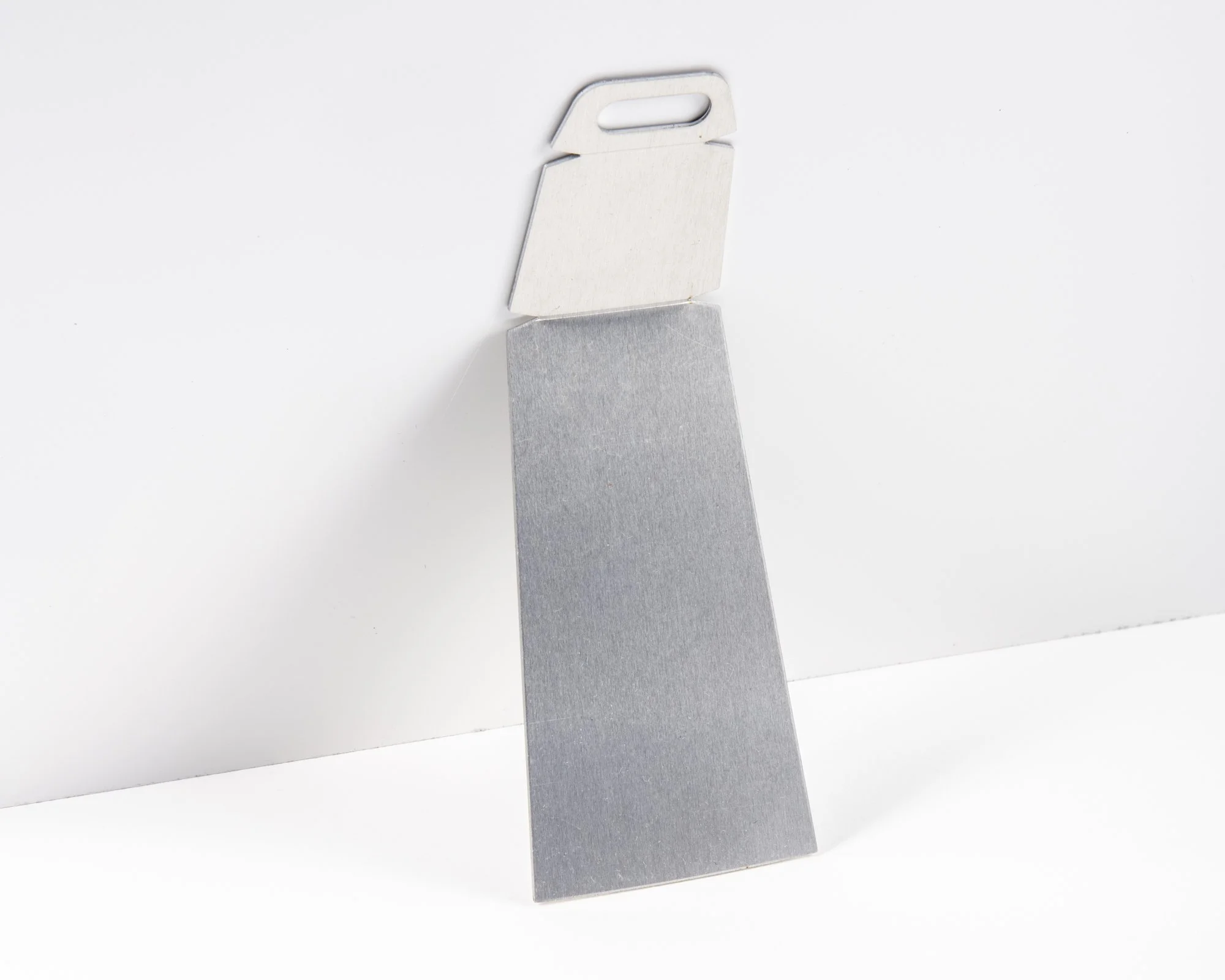 A silver metal scraper with a flat edge leaning against a white surface.