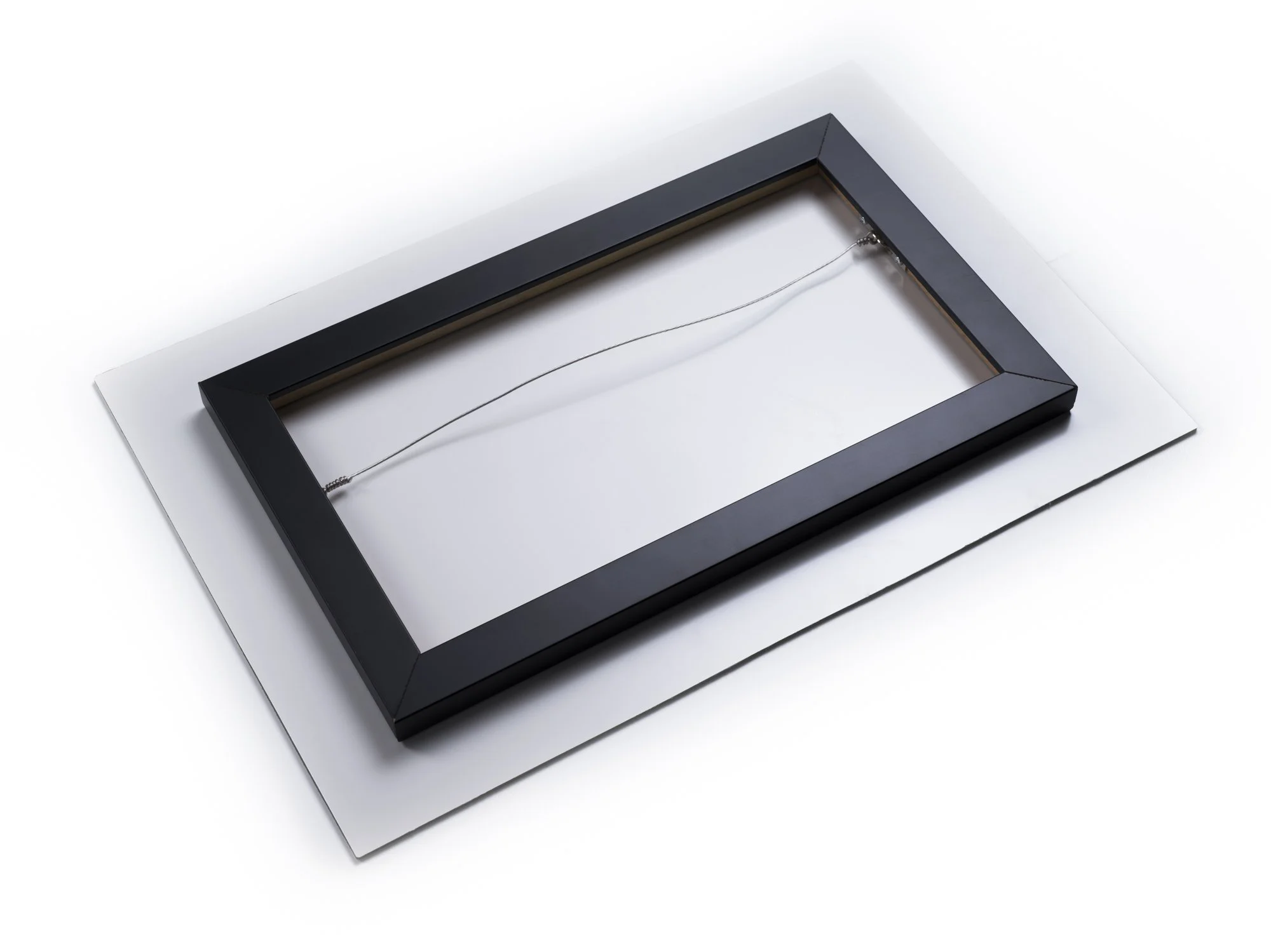 The image shows the back of a black picture frame with a wire hanger on a white surface.