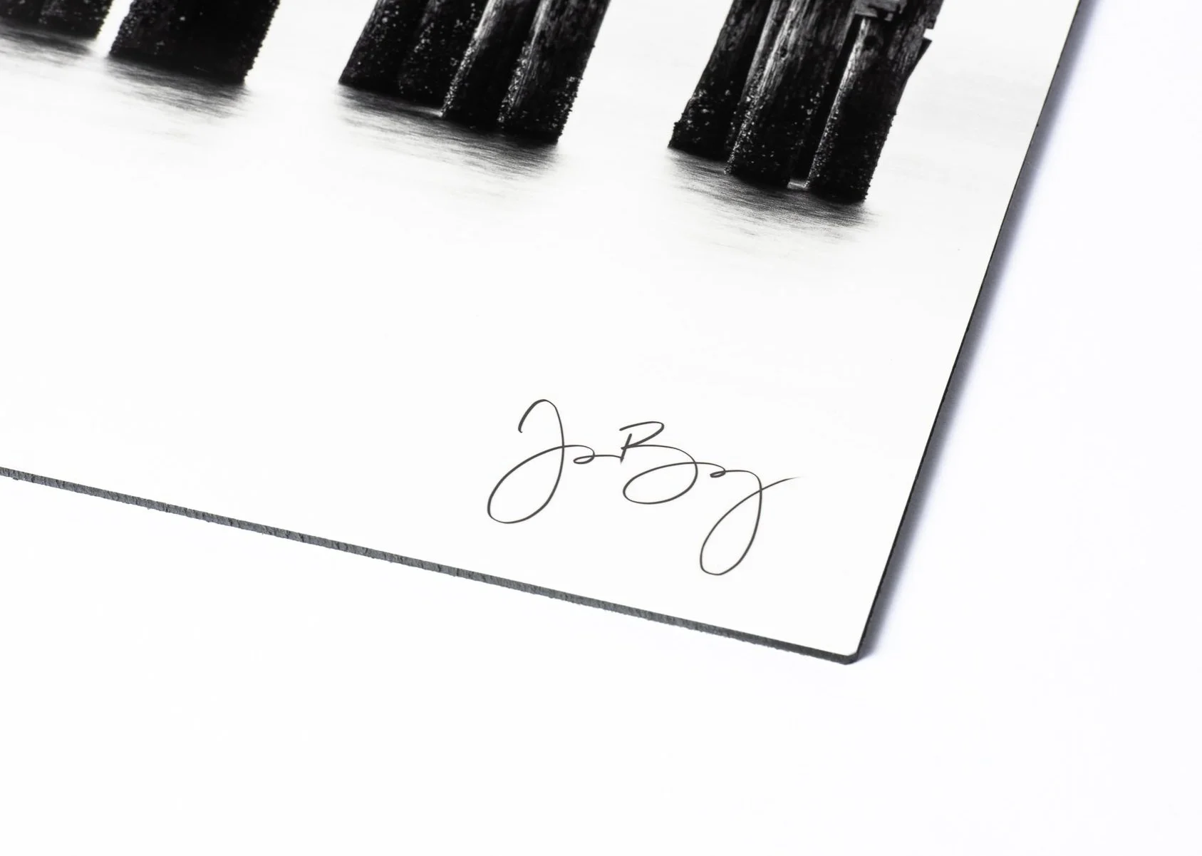 Close-up of a white card with a signature in black ink at the bottom right, and a partial black-and-white photograph of bridge supports reflected in water on the top left corner.