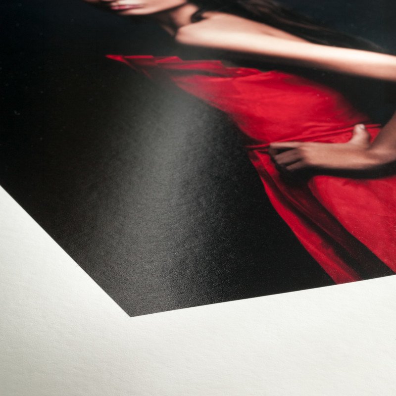 Close-up of a printed photograph or magazine page showing a person in a red dress with their hand resting on their hip, with a black background.