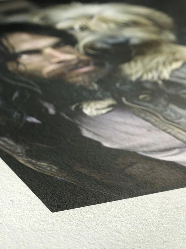 Close-up of a printed photograph showing a man with glasses and long blonde hair lying down, with part of another person's face visible, and a snake near them.