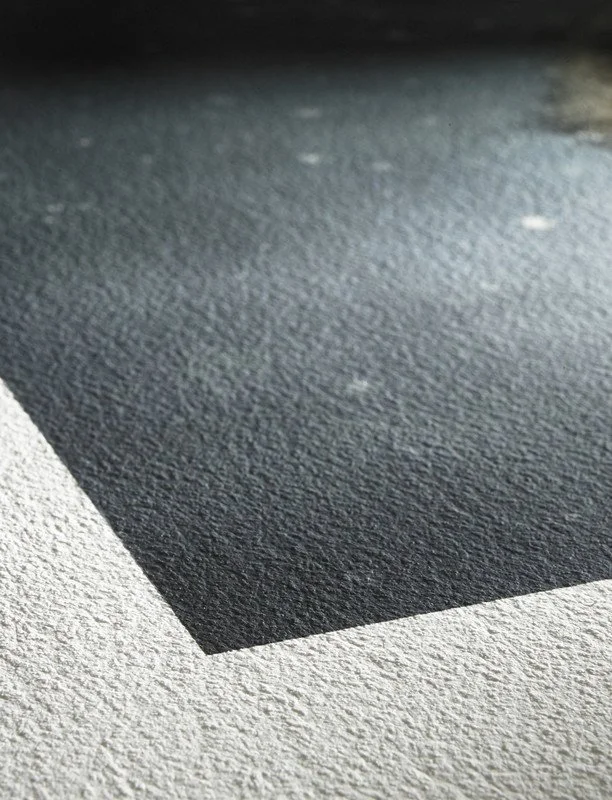 Close-up of a textured surface, possibly paper or canvas, with a black rectangular shape on it.