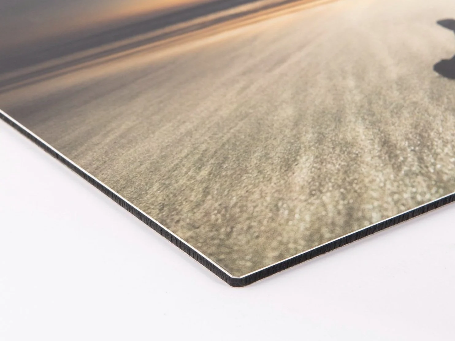 Close-up of a printed photograph with a landscape scene, showing sand dunes and a clear sky, placed on a white surface.