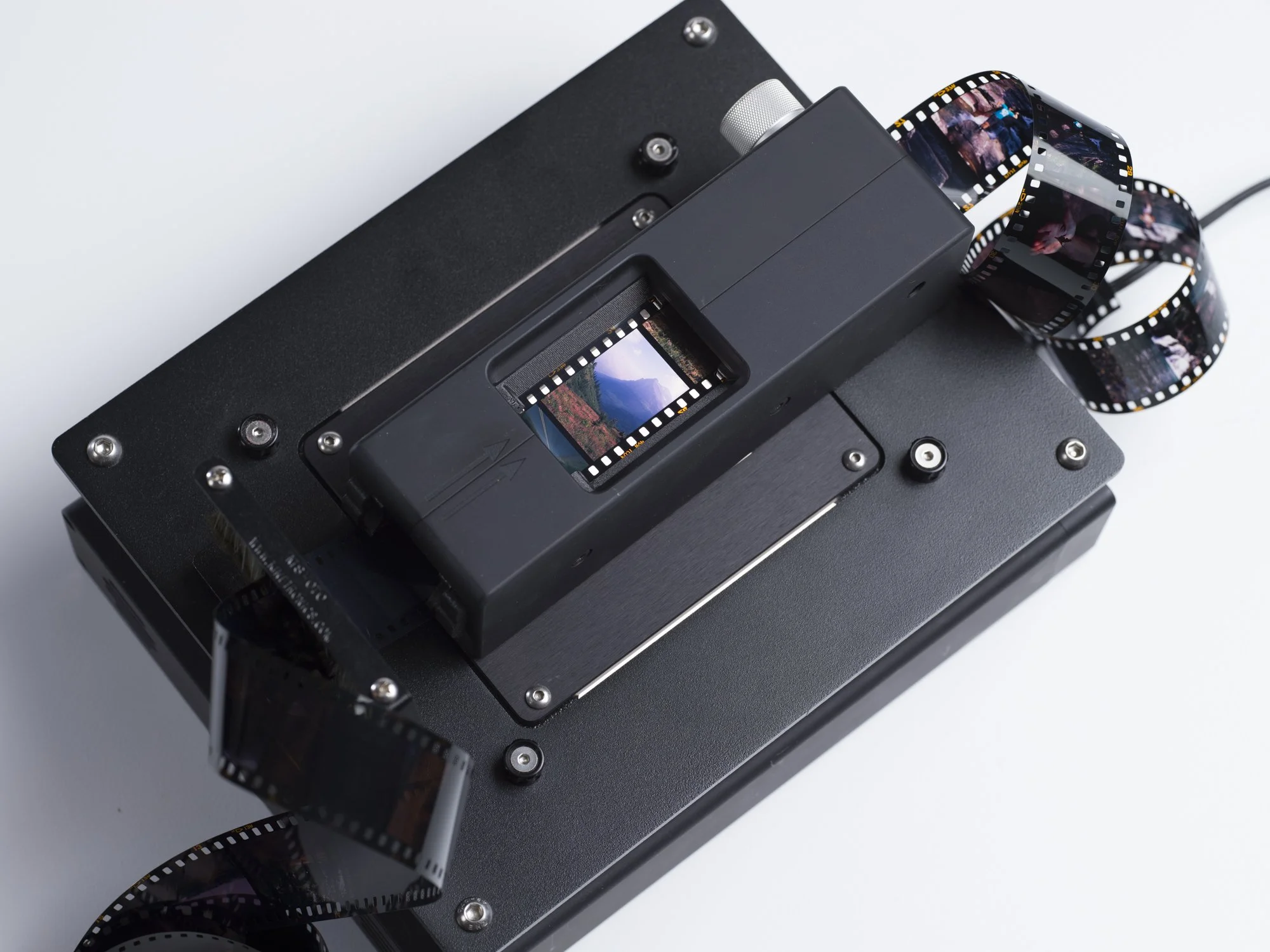 A vintage film camera with a strip of film loaded, showing a landscape scene, on a white background.