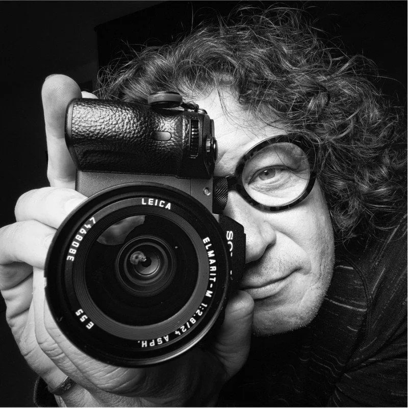 Black and white portrait of Jon McCormack holding a camera to his eye.