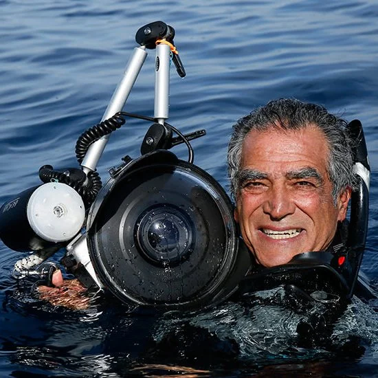 Portrait of underwater photographer Amos Nachoum holding a camera in the ocean