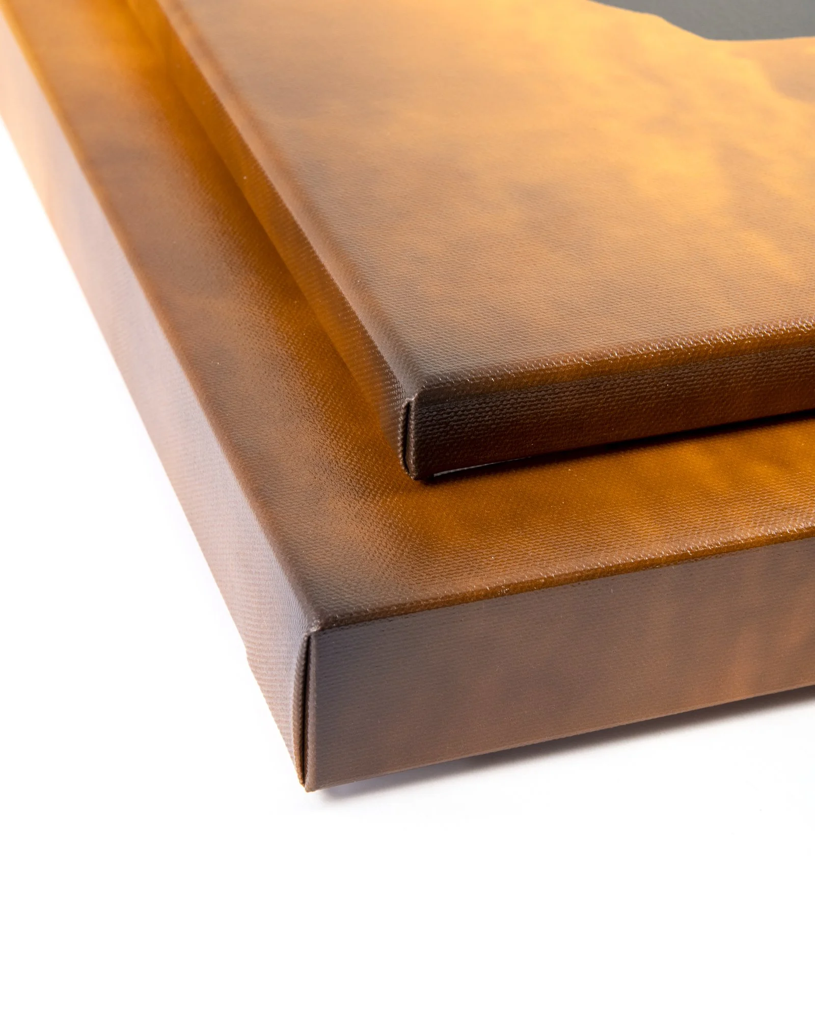 Close-up of a brown picture frame with a textured surface and a corner resting on a larger photo album or frame with matching color.