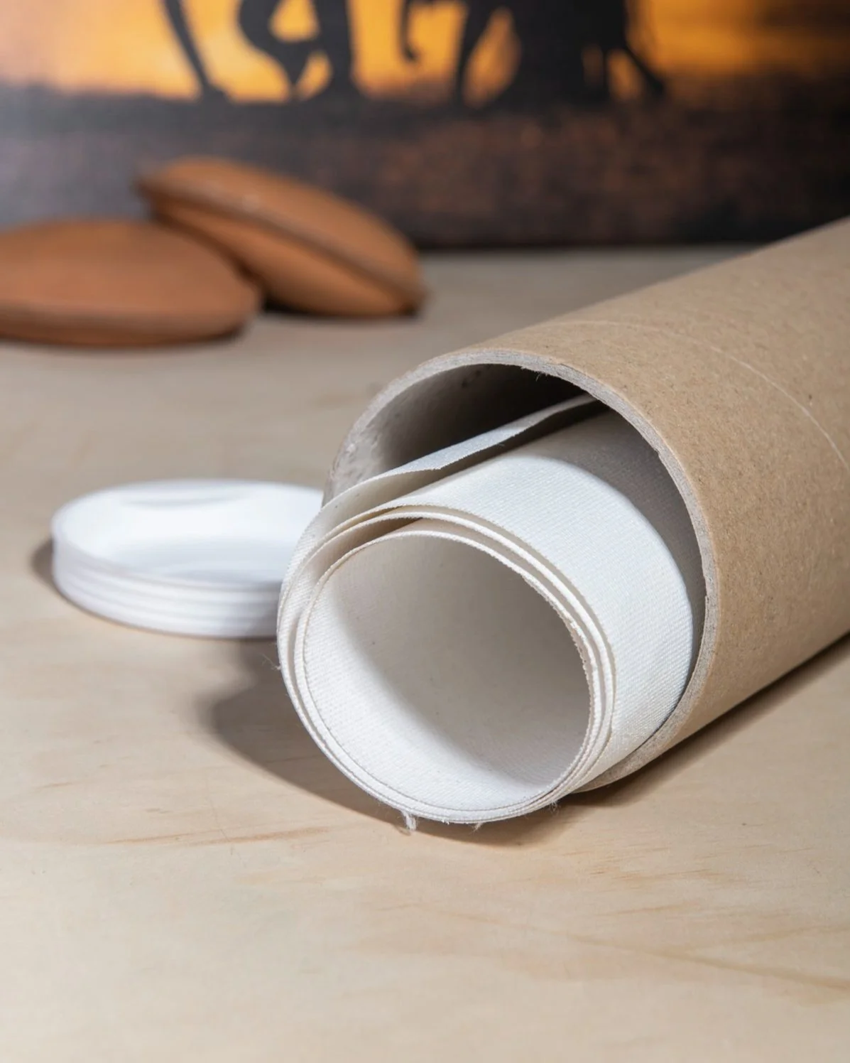 A cardboard tube containing white fabric straps resting on a wooden surface with some wooden objects in the background.