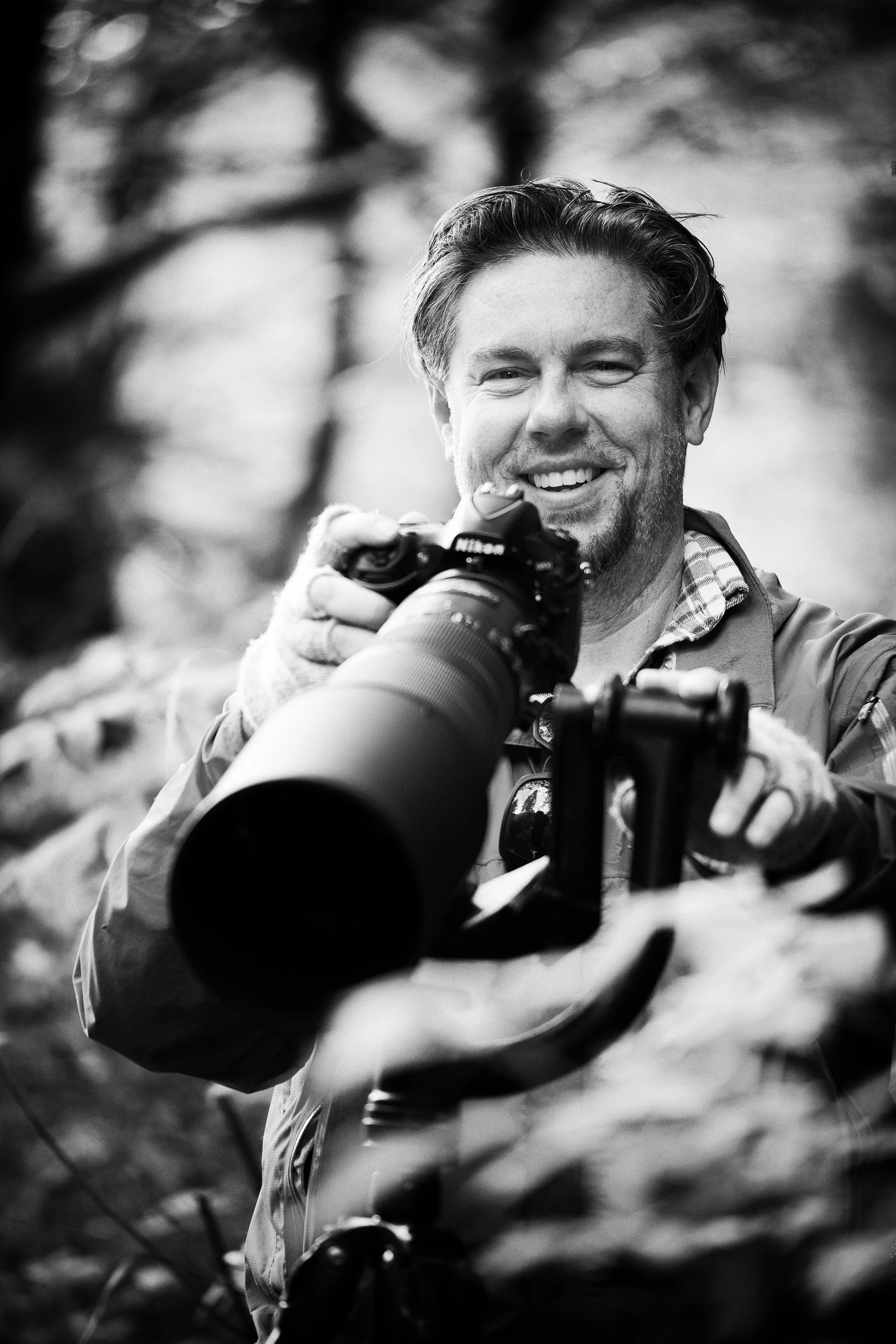 Jason Bradley, CEO and founder, holding a camera with a large telephoto lens while smiling outdoors.