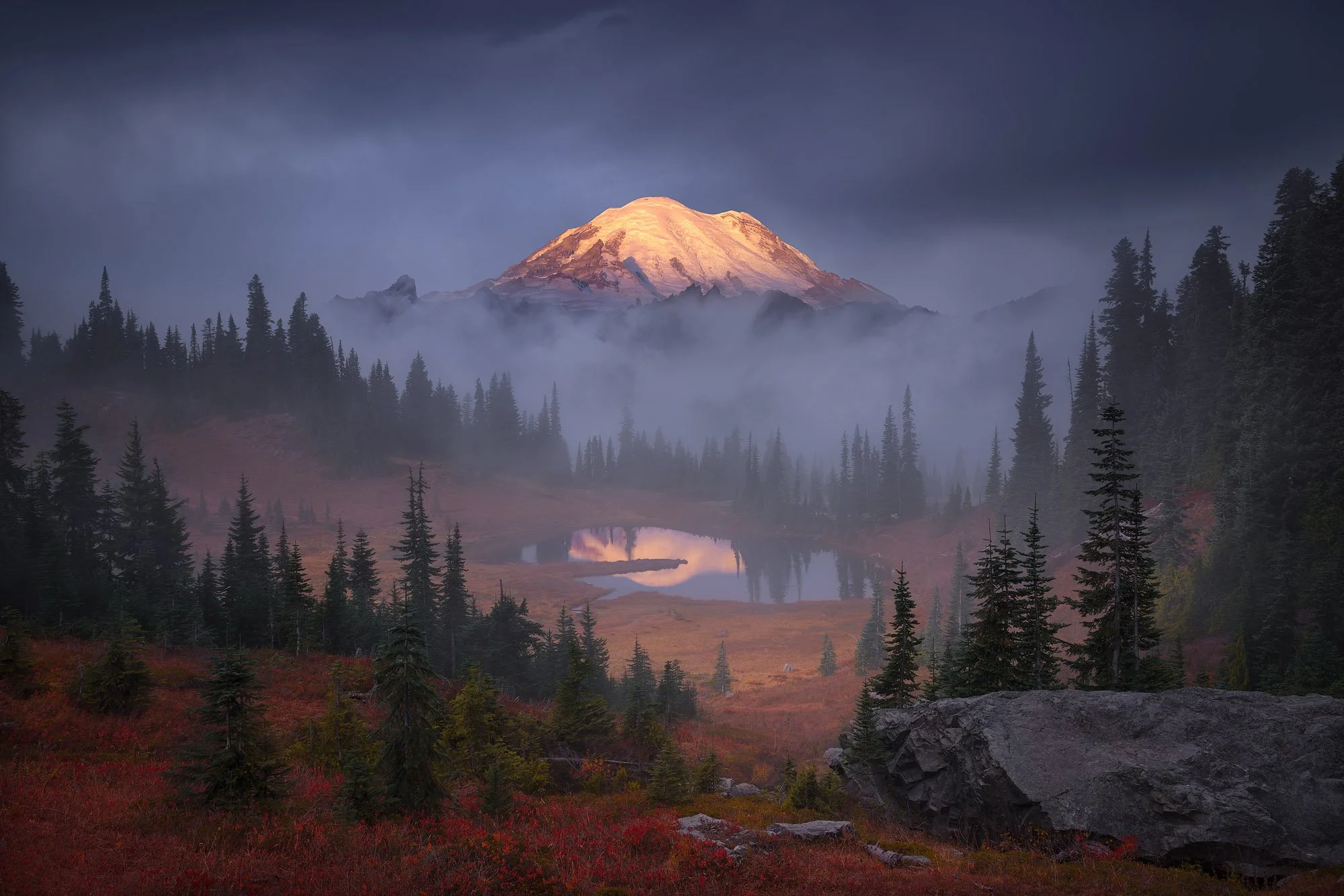 Misty autumn landscape with glowing volcanic peak and alpine lake, photographed by Alex Noriega.