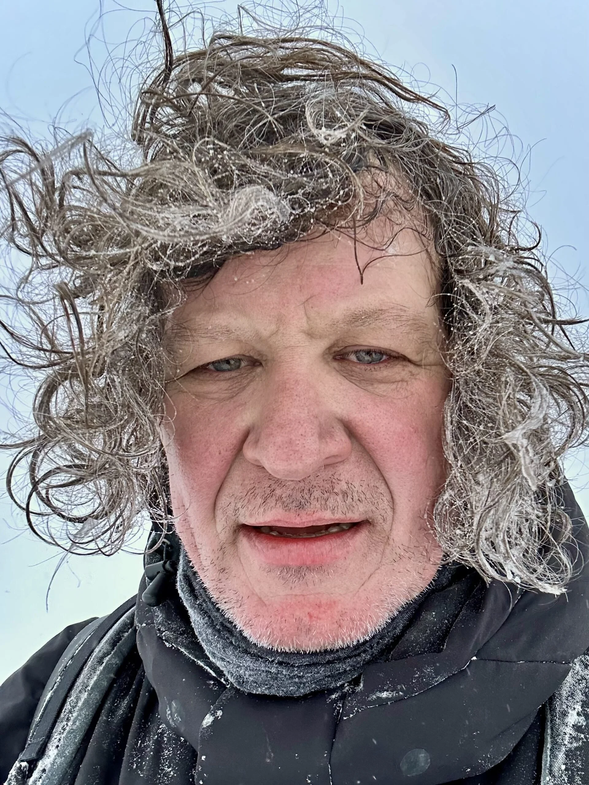 Portrait of photographer Jon McCormack outdoors in cold weather with windblown hair.