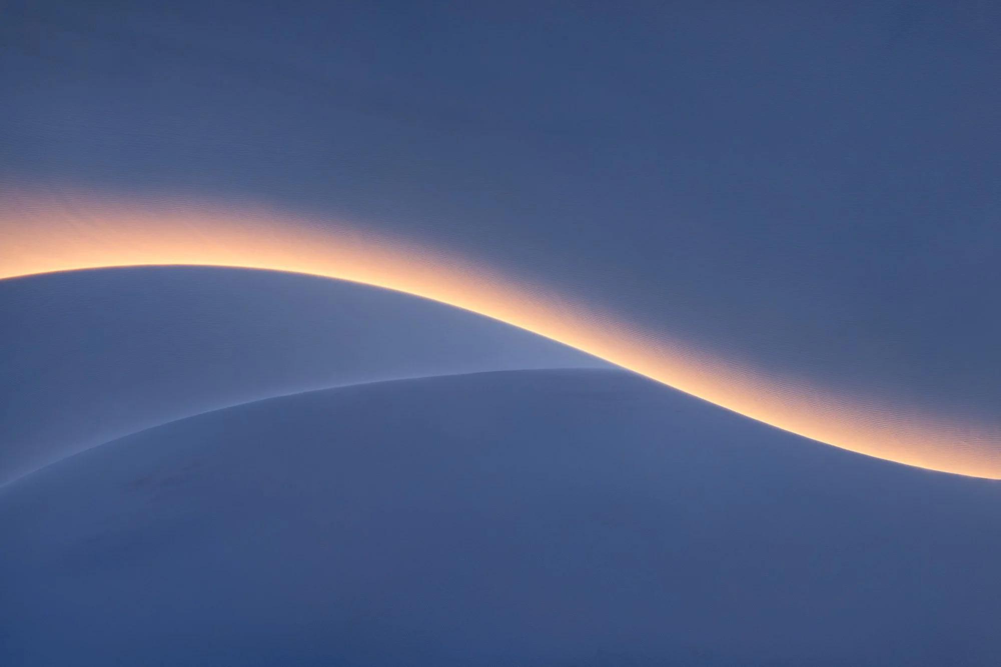 Minimalist desert sand dunes with a glowing golden ridge line at sunrise, photographed by Alex Noriega.