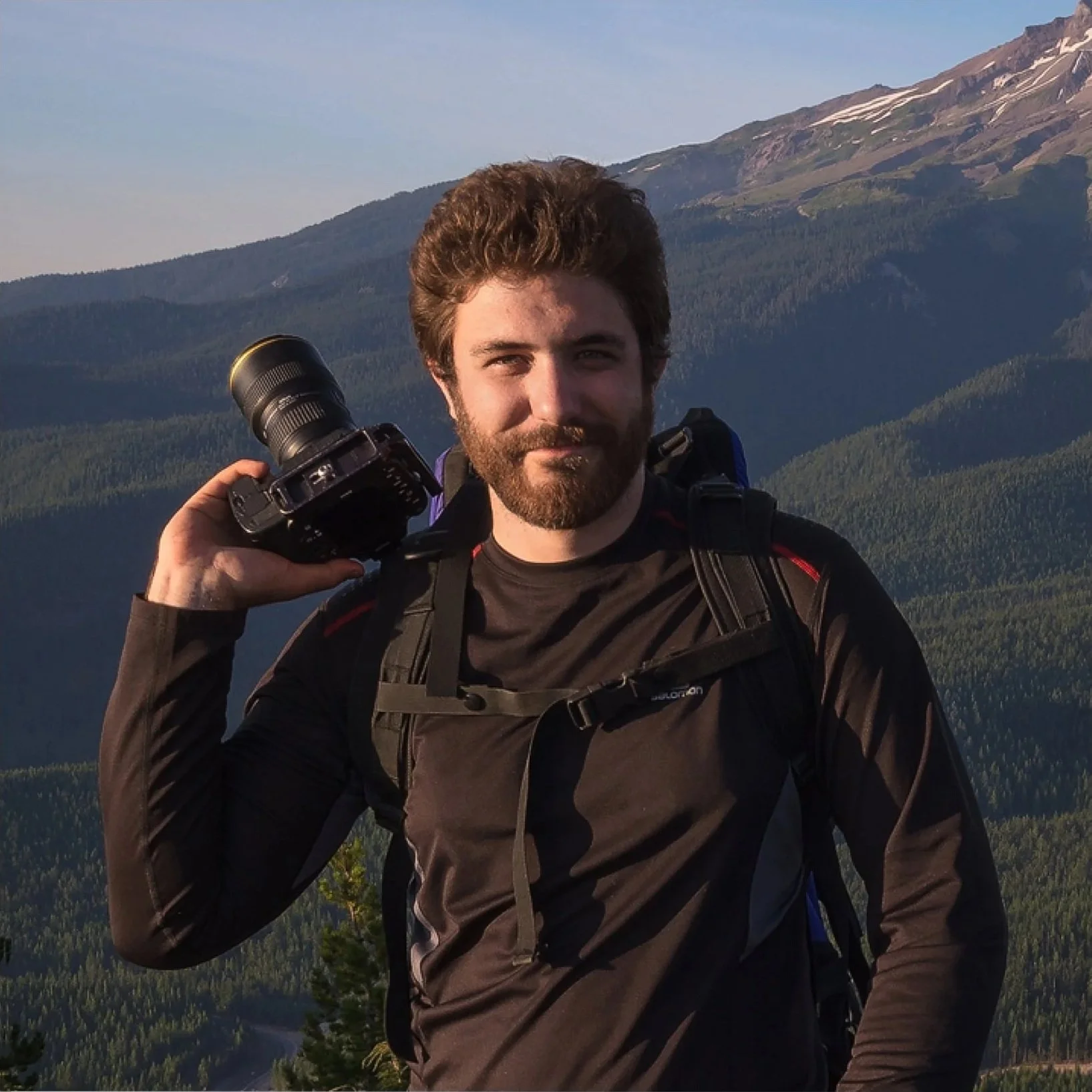 Photographer Alex Noriega holding a camera outdoors in a mountainous landscape.