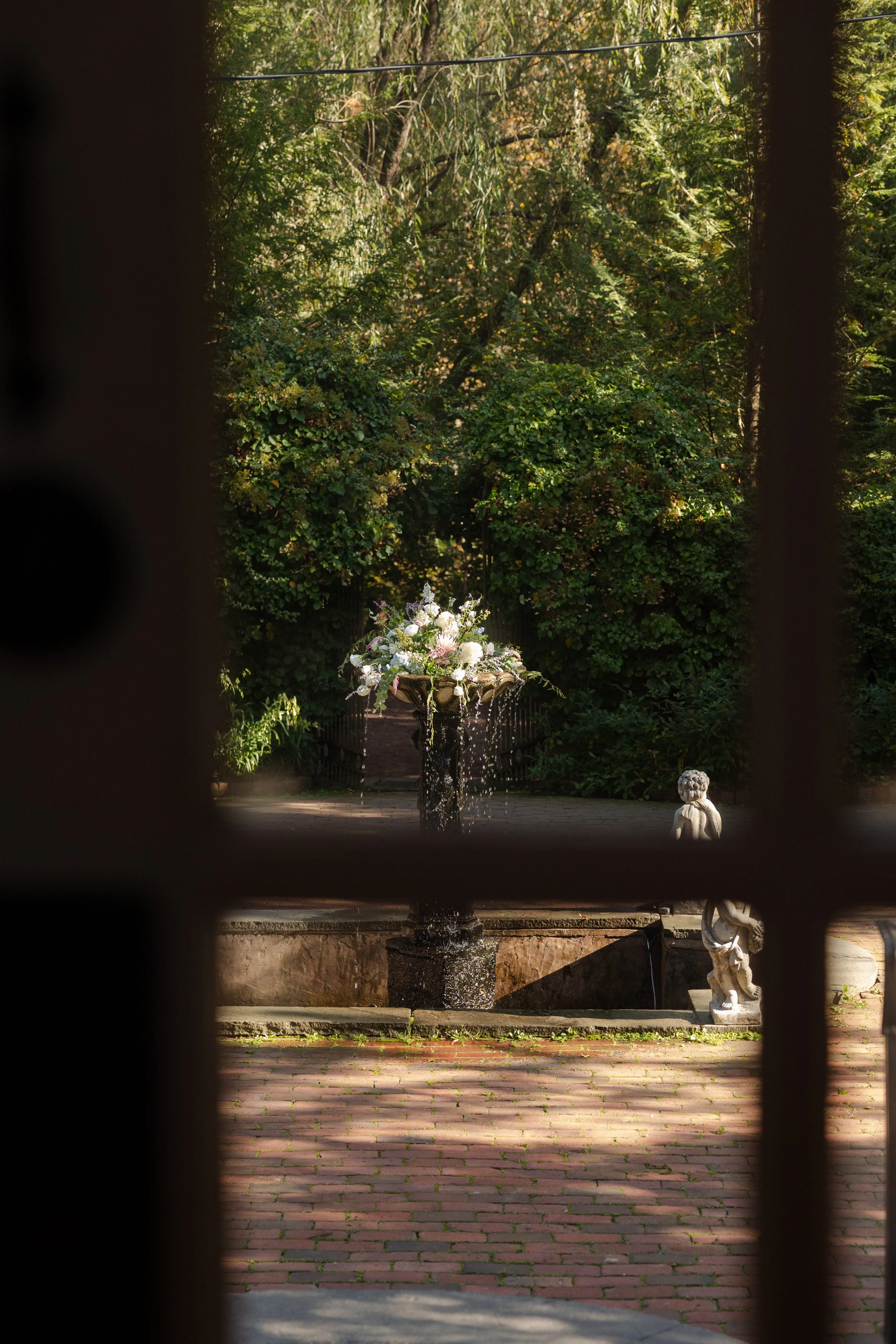 A decorative fountain with a bouquet of flowers at the top, water flowing down, surrounded by greenery and trees for a wedding in Somerville, New Jersey photographed by Dominique Paulette Photography